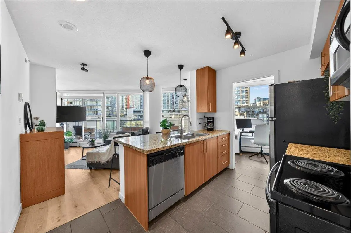 Open-concept condo with wood cabinets, granite countertops, and stainless steel appliances. Living room with balcony and city view.