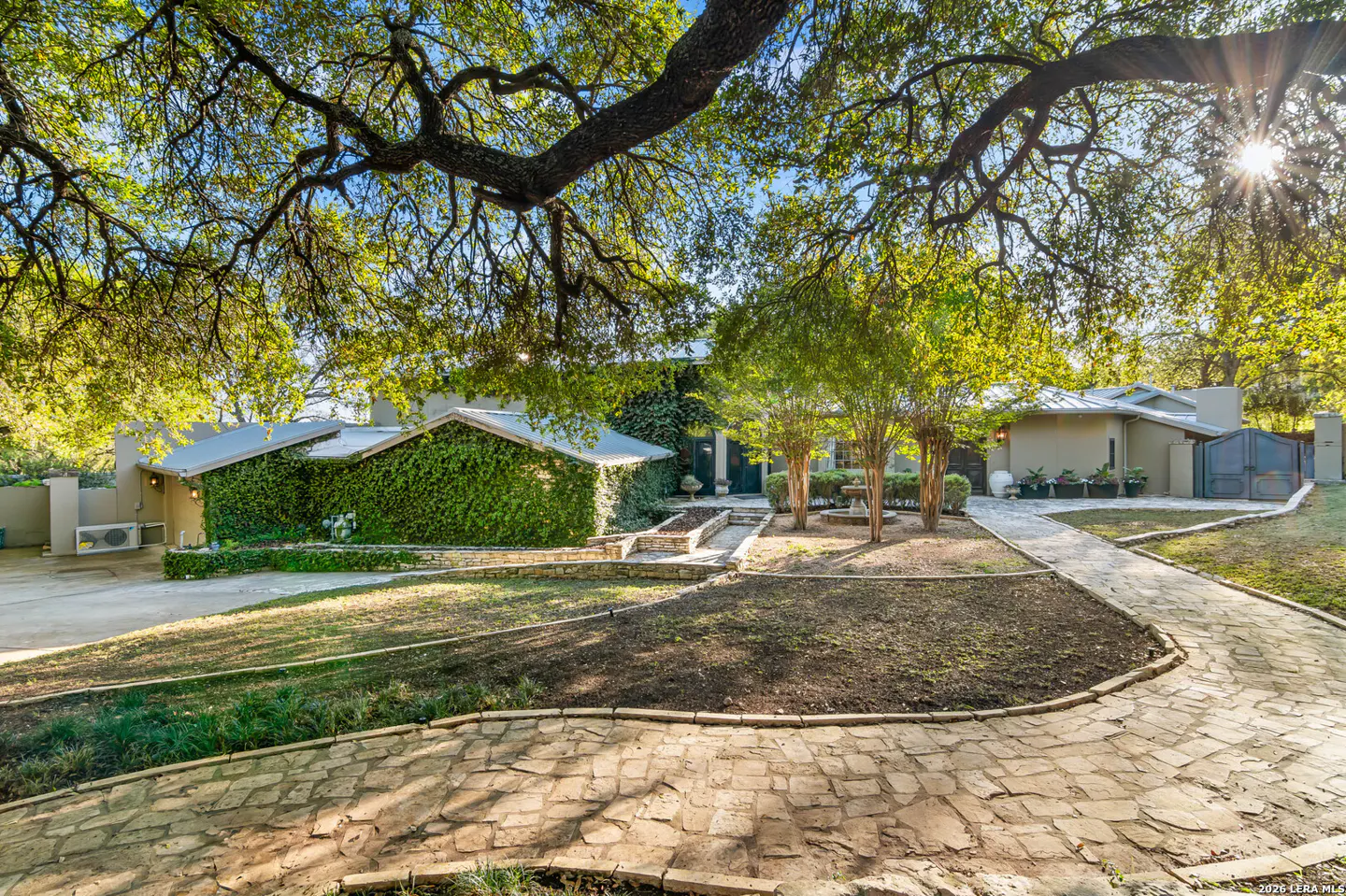 Exterior of a home with a stone path, green lawn, and ivy-covered walls under a large tree.