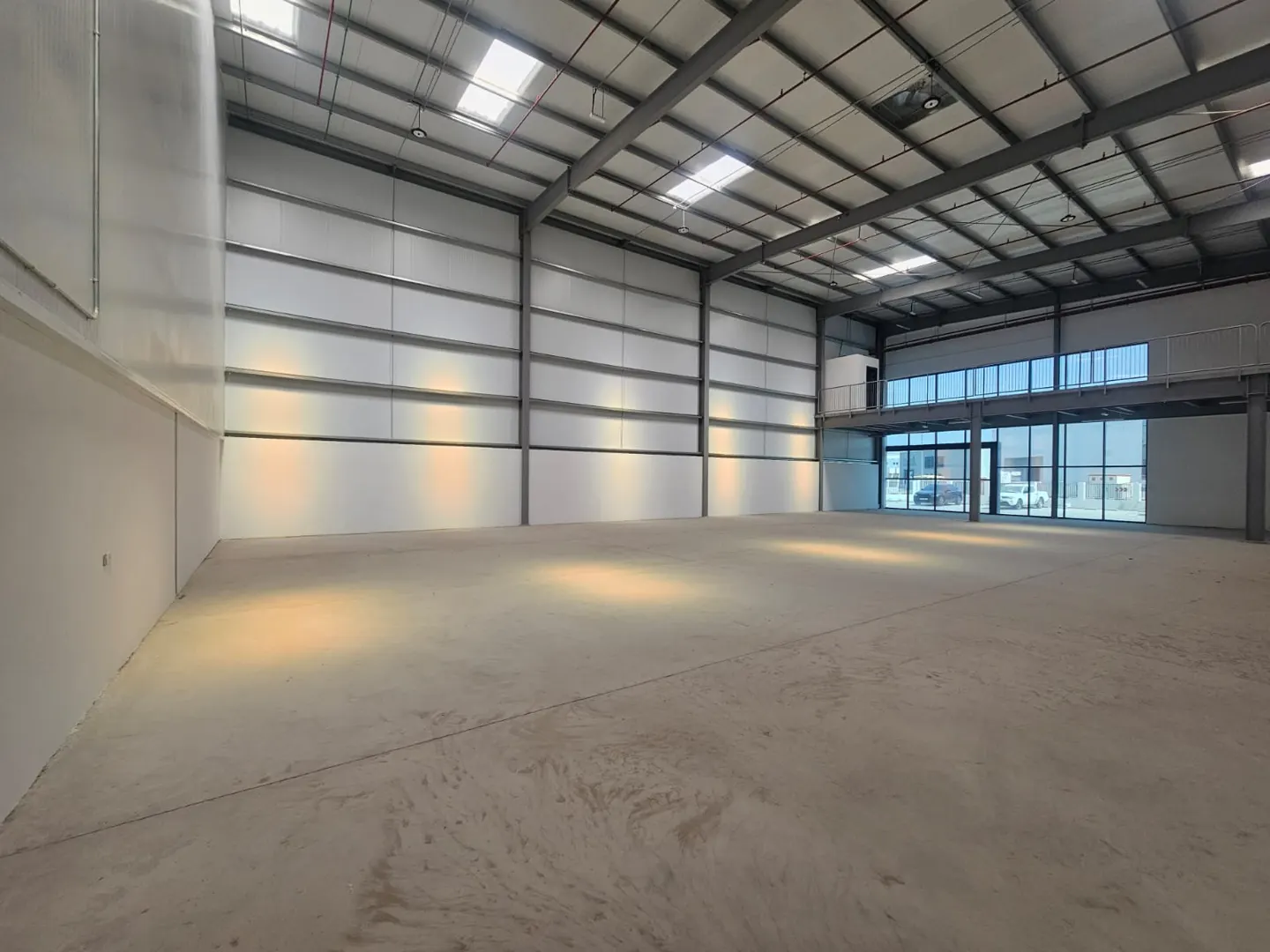 A large, empty warehouse with a concrete floor, metal walls, and a mezzanine office space.