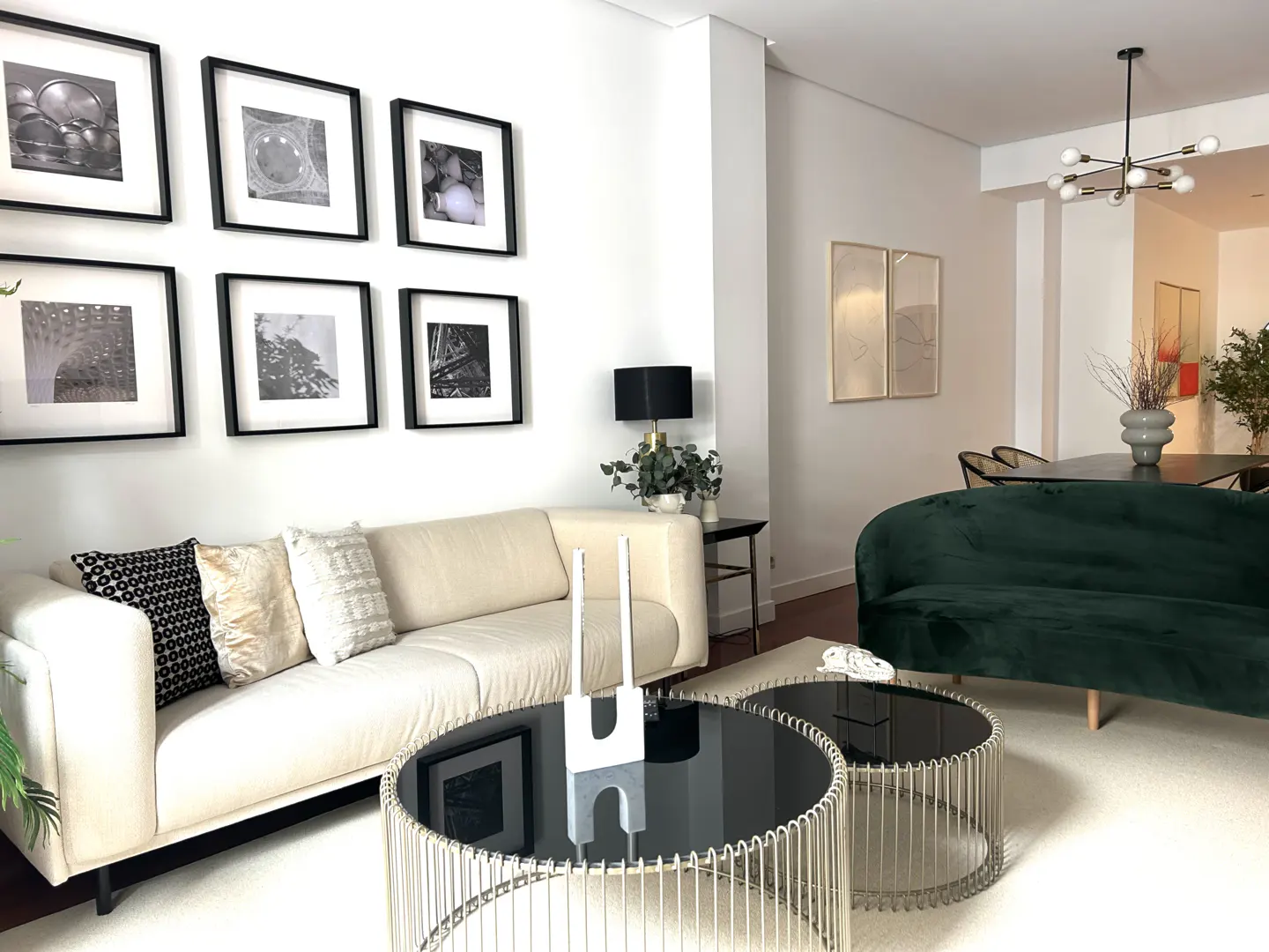 Modern living room with a cream sofa, dark green velvet couch, two round glass coffee tables, and gallery wall art.