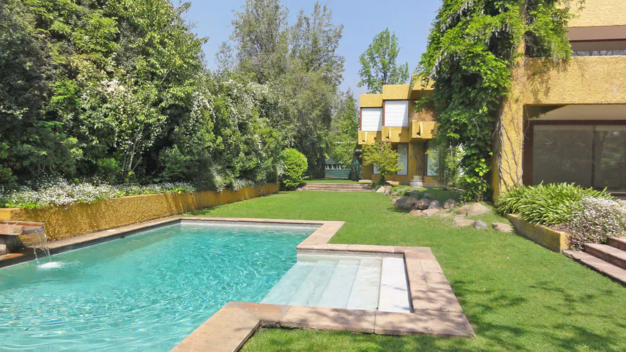 A backyard with a turquoise pool, green lawn, and a yellow house with climbing vines.