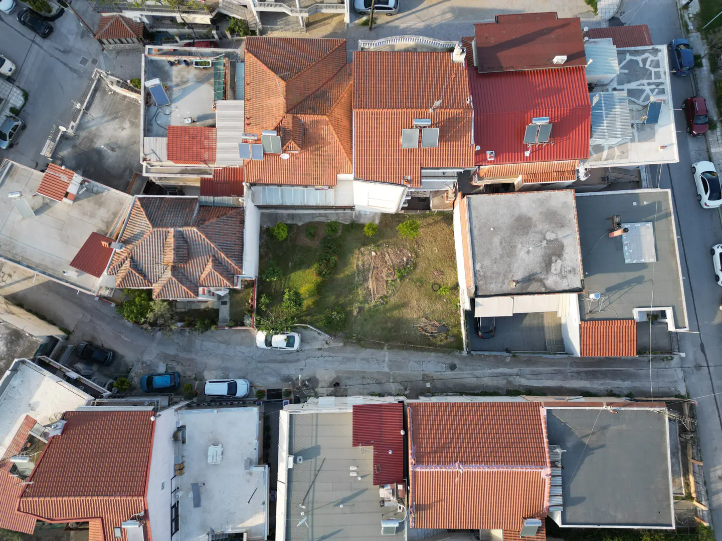 Aerial view of a neighborhood with red-tiled roofs, green yards, and parked cars on the streets.