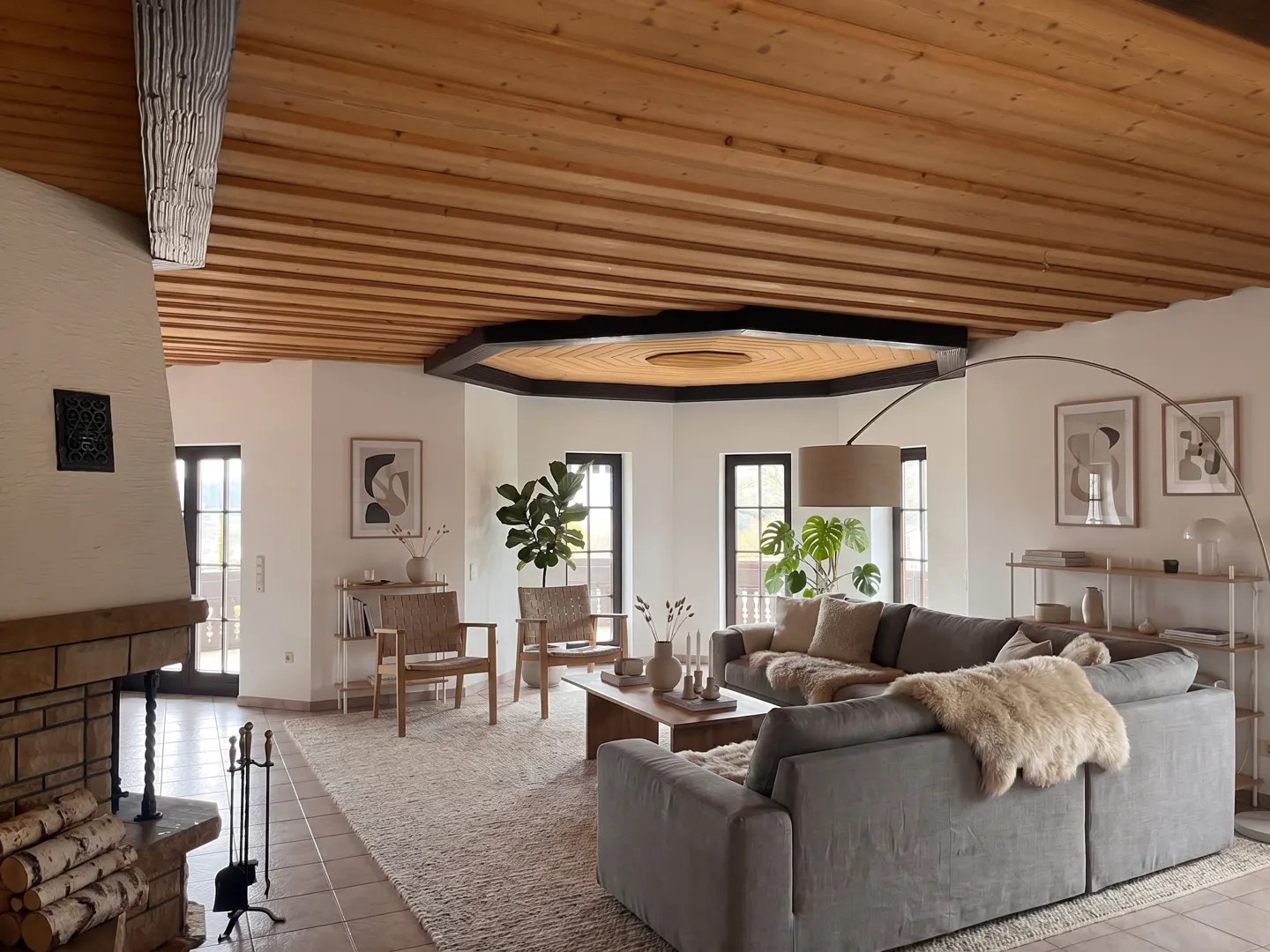 A living room with a stone fireplace, wood ceiling, gray sofa, woven chairs, and a light rug.