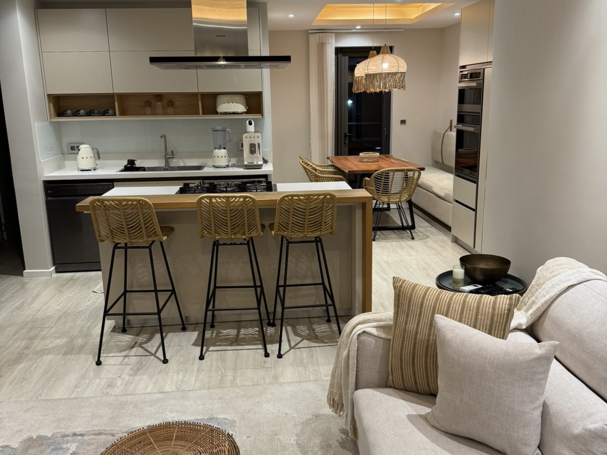 Modern open-plan kitchen with a breakfast bar, rattan stools, dining area, and a cozy living room with a beige sofa. [AI-generated text]