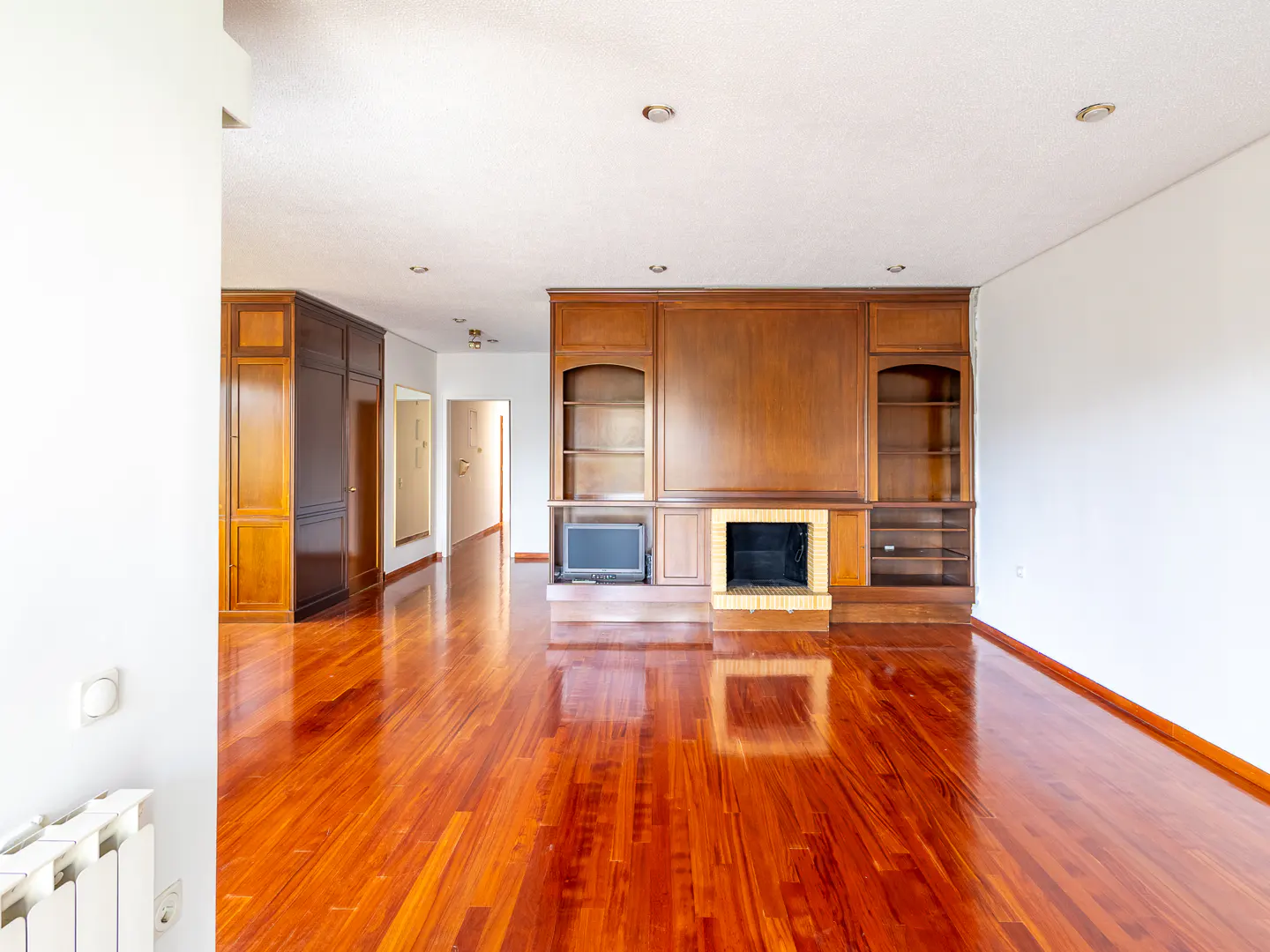 Spacious living room with polished hardwood floors, a large wooden wall unit with built-in shelving, and a fireplace.