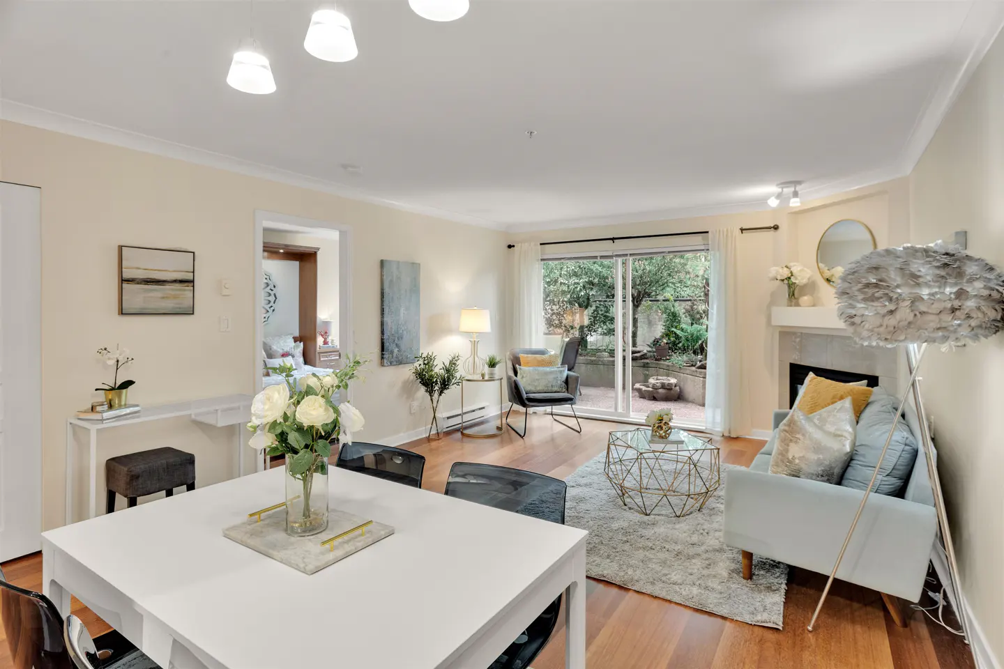 Bright, open-concept living and dining area with hardwood floors. White dining table, light blue sofa, fireplace, and sliding glass doors to a patio.