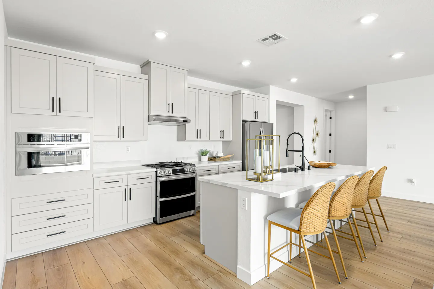 Bright, modern kitchen with white cabinets, stainless steel appliances, and a marble island with four woven bar stools.