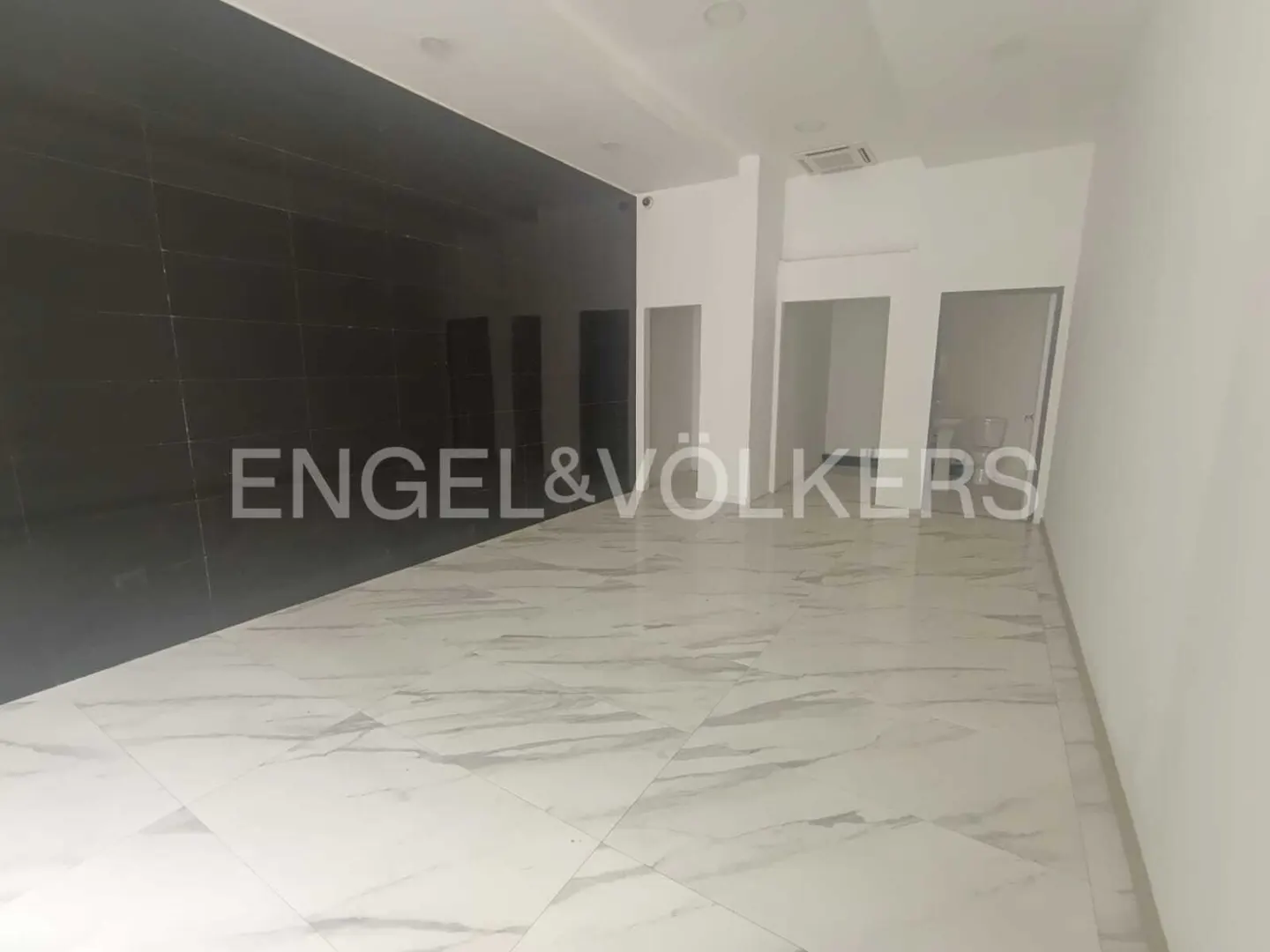 Empty commercial space with white marble floors, black tiled wall, and white walls with door openings.