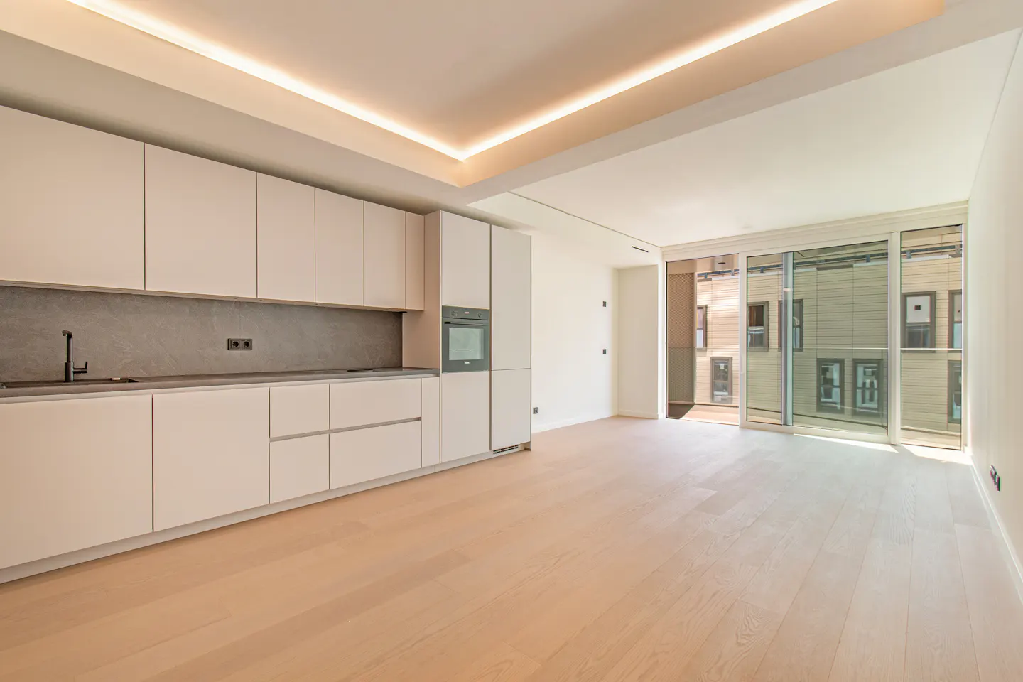 Bright, modern kitchen with white cabinets, gray backsplash, and light wood floors. Large sliding glass doors lead to a balcony.