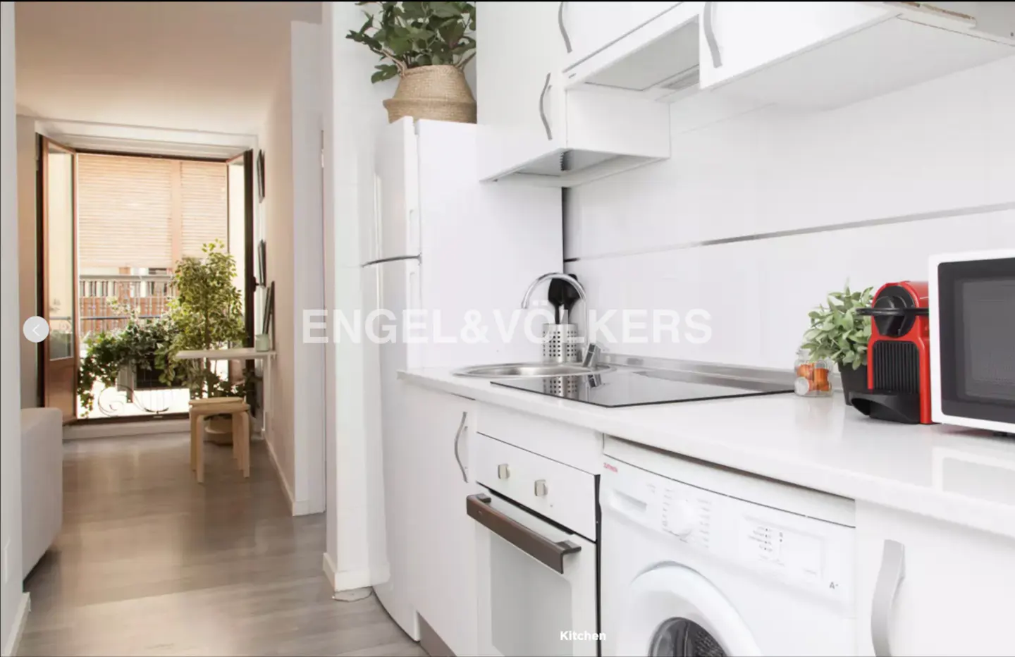Bright, modern kitchen with white cabinets, appliances, and countertops. A balcony with plants is visible through an open doorway.