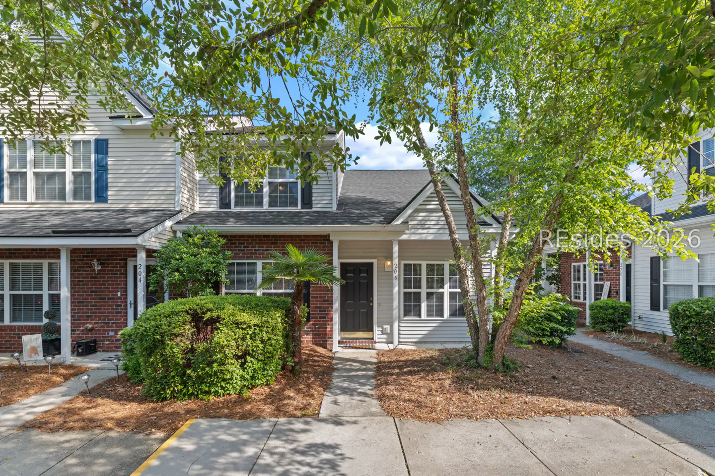 A two-story townhouse with gray siding, a black door, and green bushes in front.