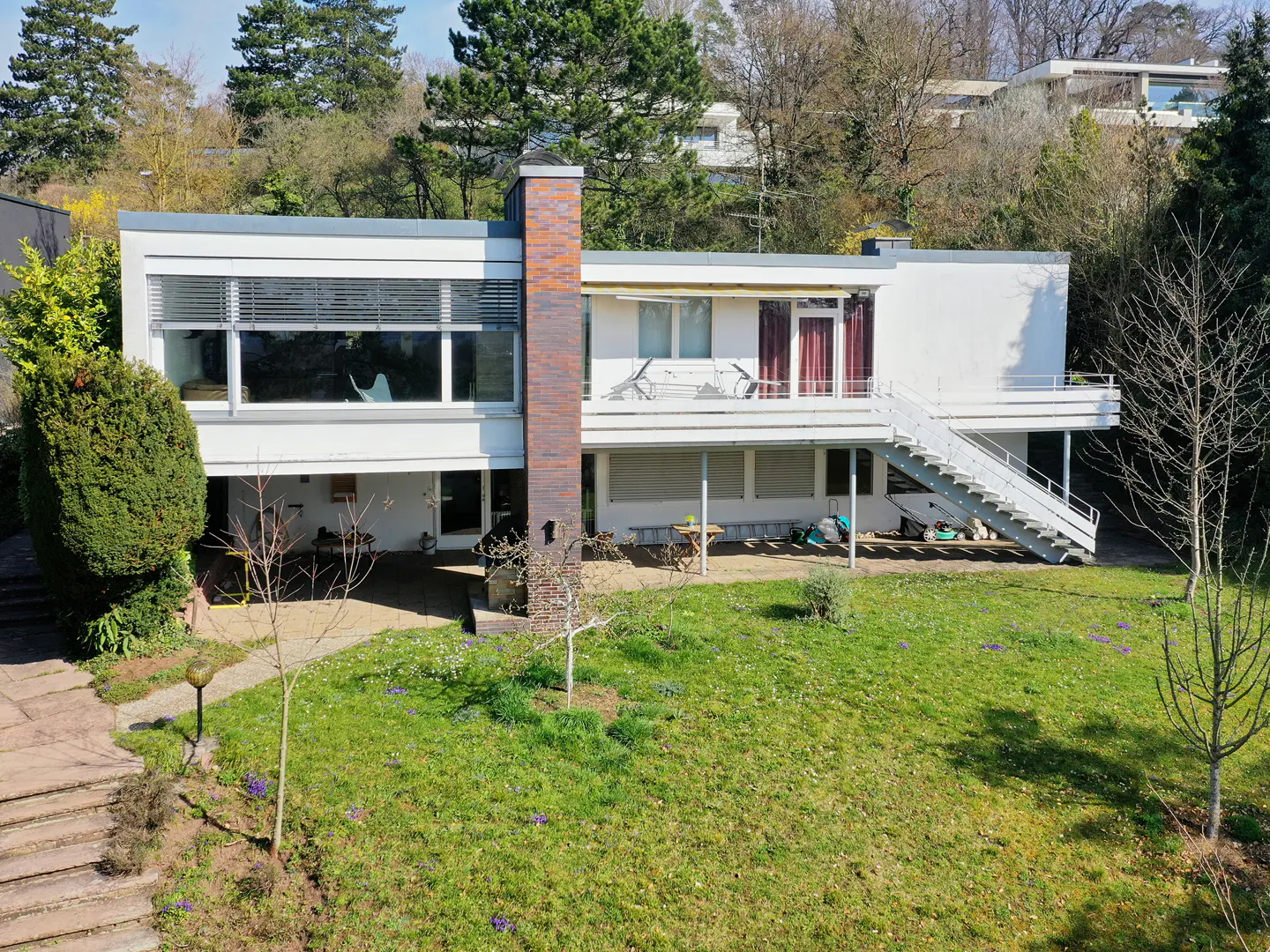 Modern white house with a brick chimney, a balcony, and a staircase leading to the lawn.