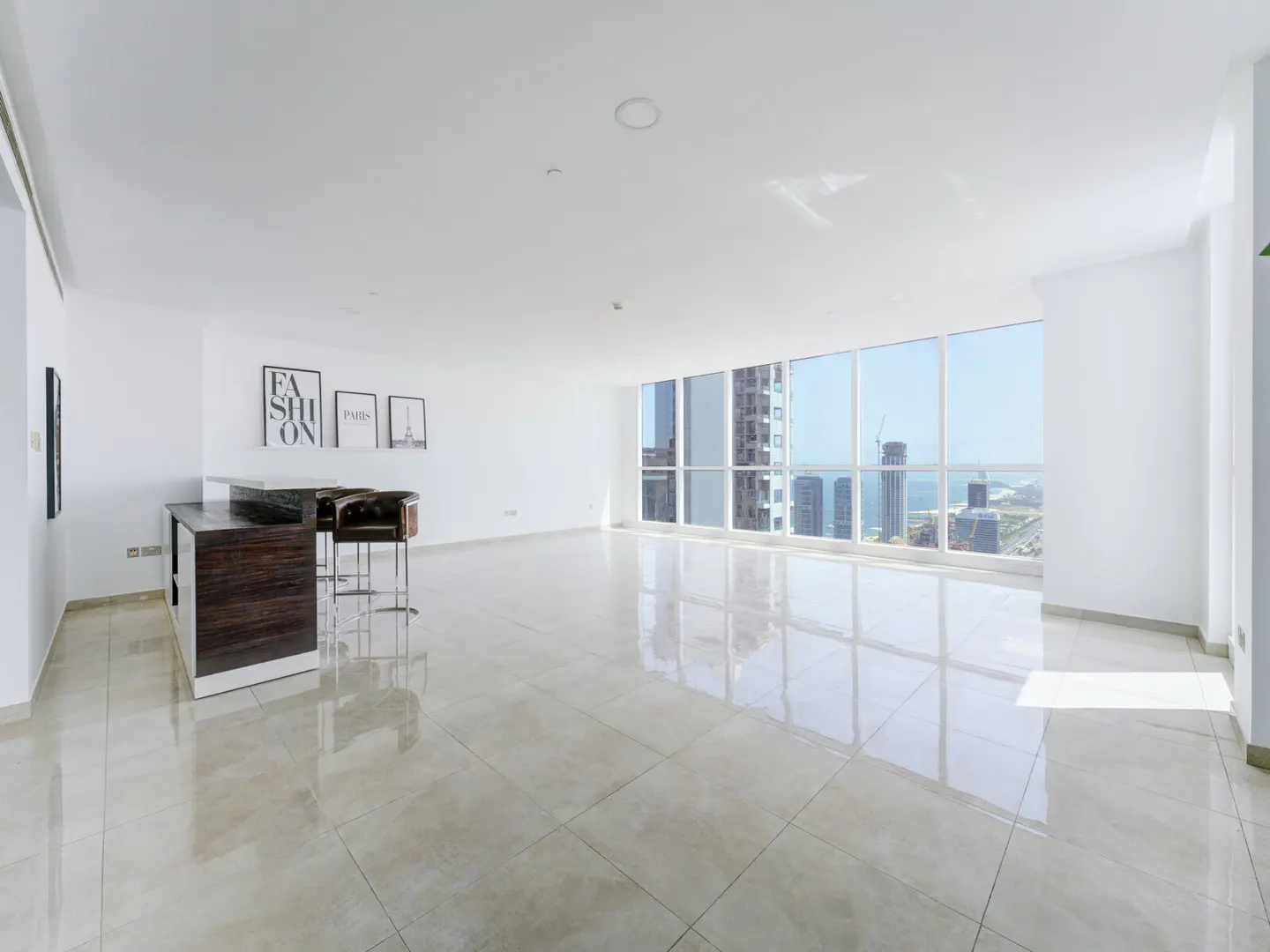 Modern white living room with a dark wood breakfast bar, two stools, wall art, and floor-to-ceiling windows with city views.