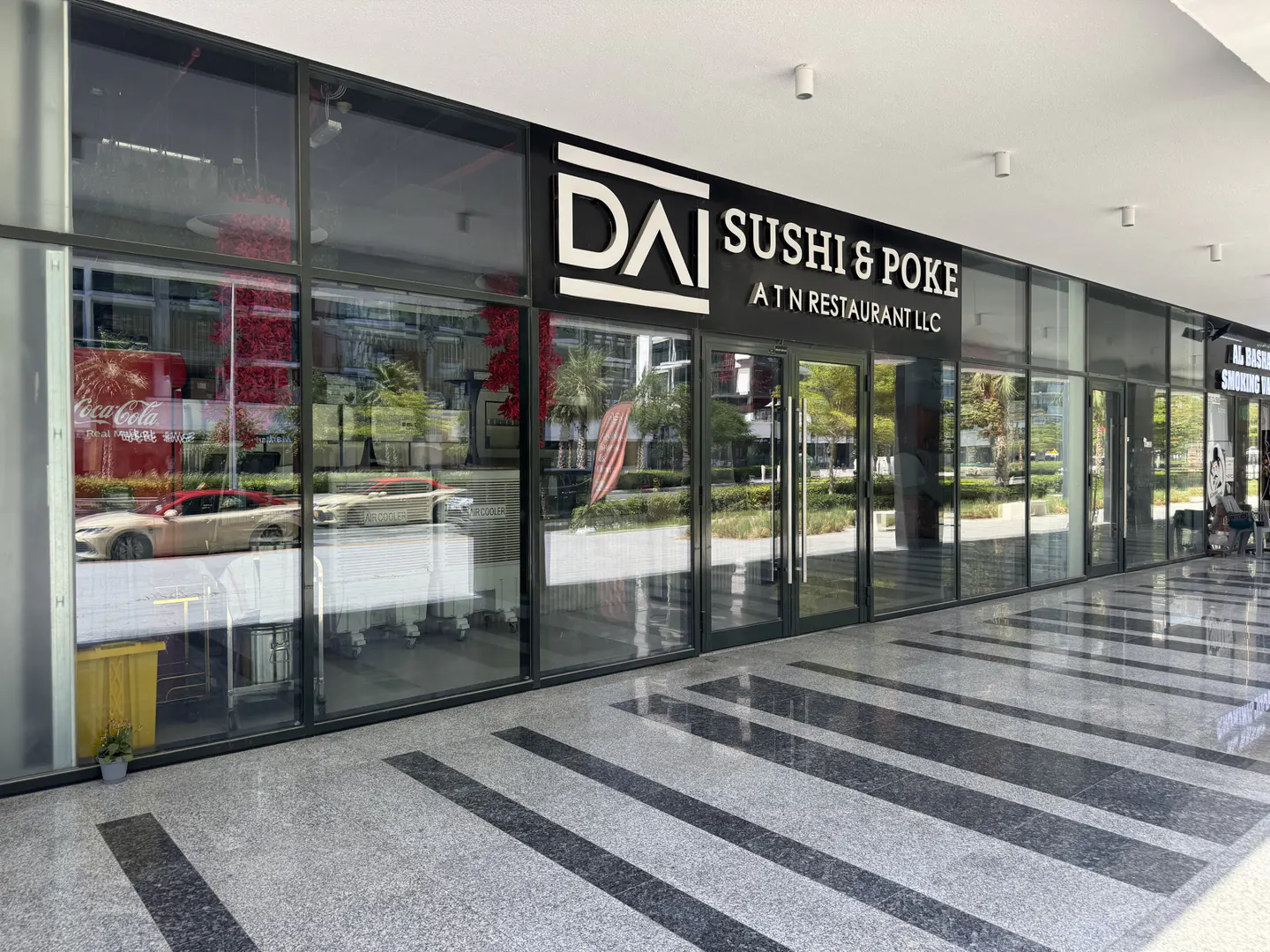 Exterior view of "DAI Sushi & Poke" restaurant with glass windows and doors. The floor is gray with black stripes.