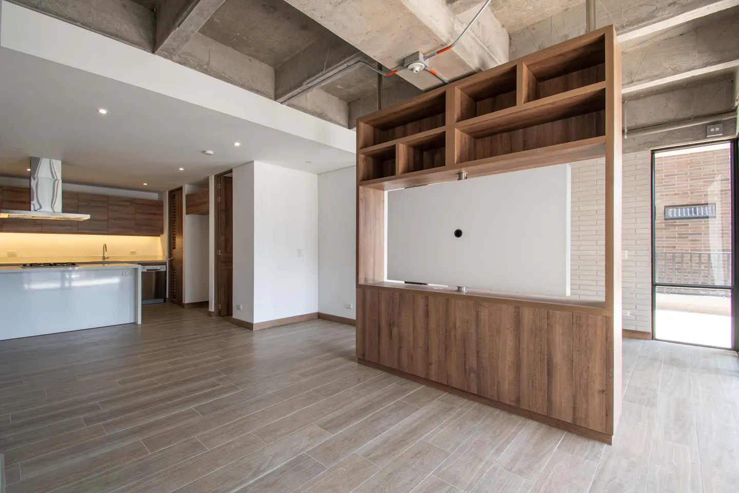 Open-concept living space with wood floors, a kitchen with a white island, and a wood entertainment center with shelves.