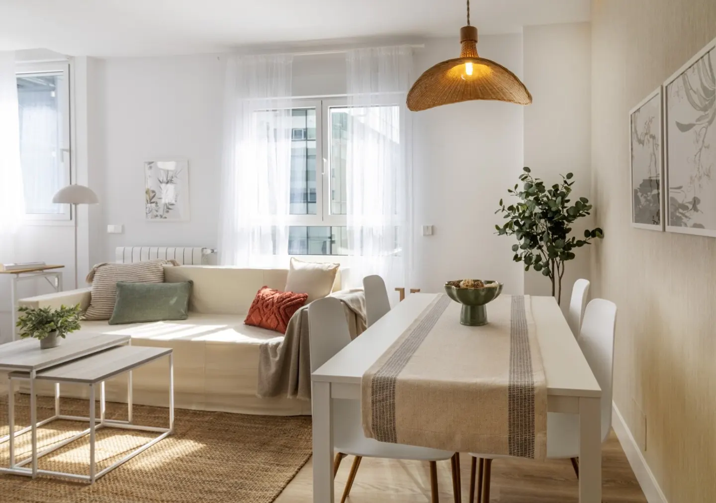 Bright, modern living and dining area with white walls, a sofa, and a white dining table with four chairs. A woven pendant light hangs above.