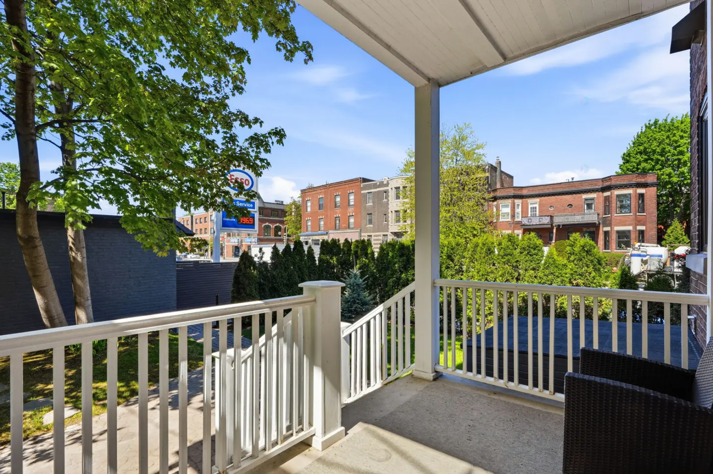 View from a porch with white railings, overlooking a street with buildings and an Esso gas station.