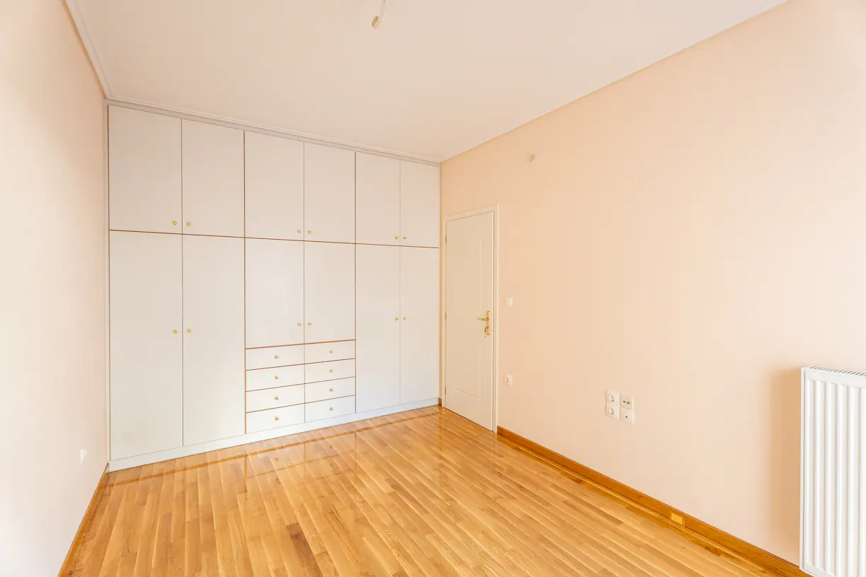 Bright bedroom with hardwood floors, peach walls, and a large white built-in wardrobe. A white door and radiator are also visible.