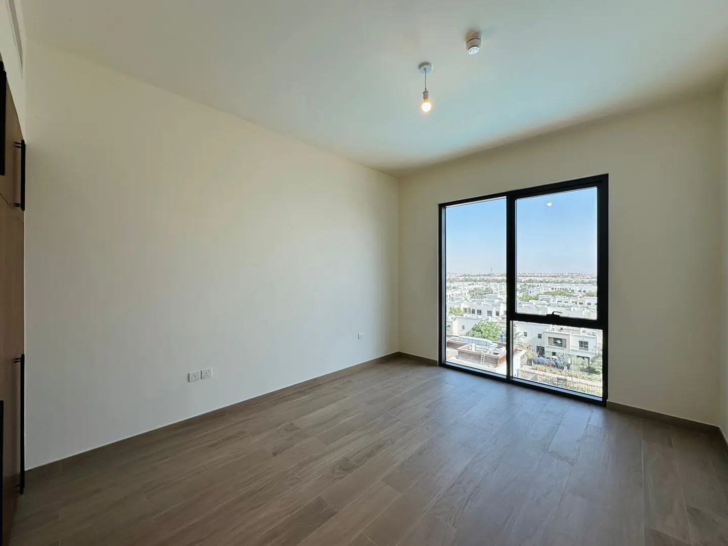 Bright, empty room with wood-look tile floor, cream walls, and a large window with a city view.