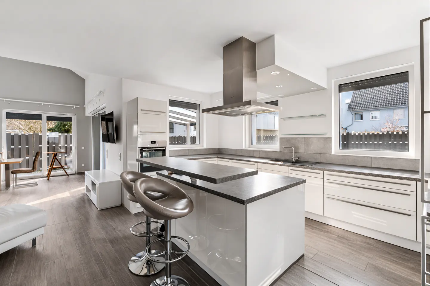 Bright, modern kitchen with white cabinets, gray countertops, and stainless steel appliances. Island with bar stools and open living area.