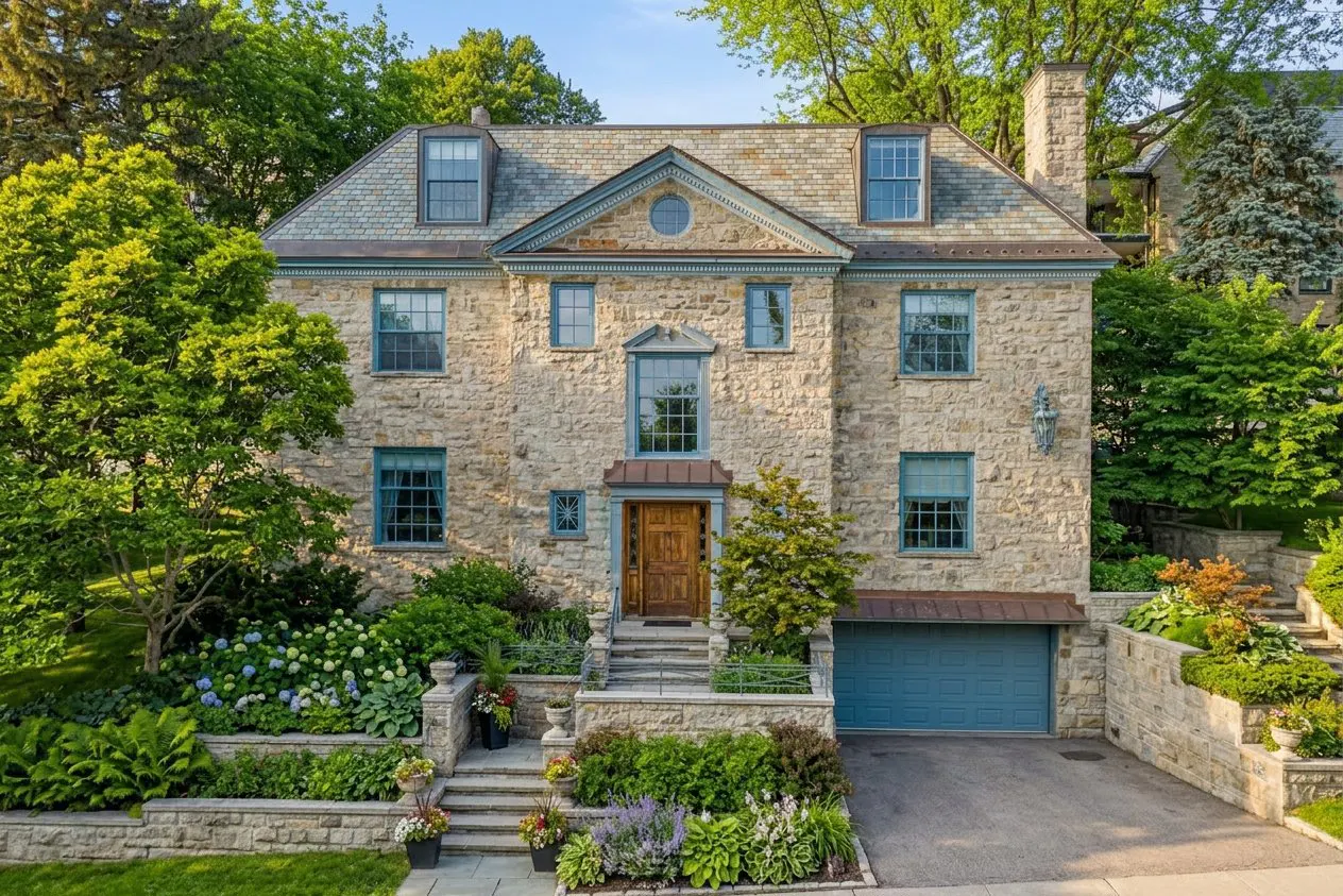 Stone house with blue trim, a brown door, and a blue garage door. The house is surrounded by green trees and bushes.
