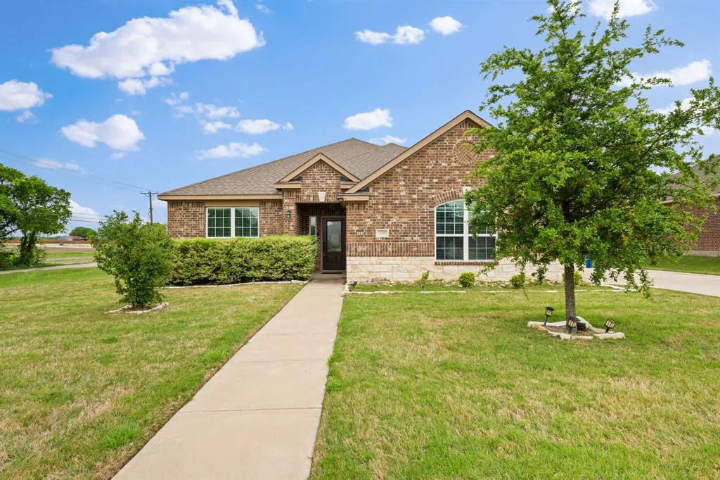 A single-story brick house with a brown roof, green lawn, and blue sky with white clouds.