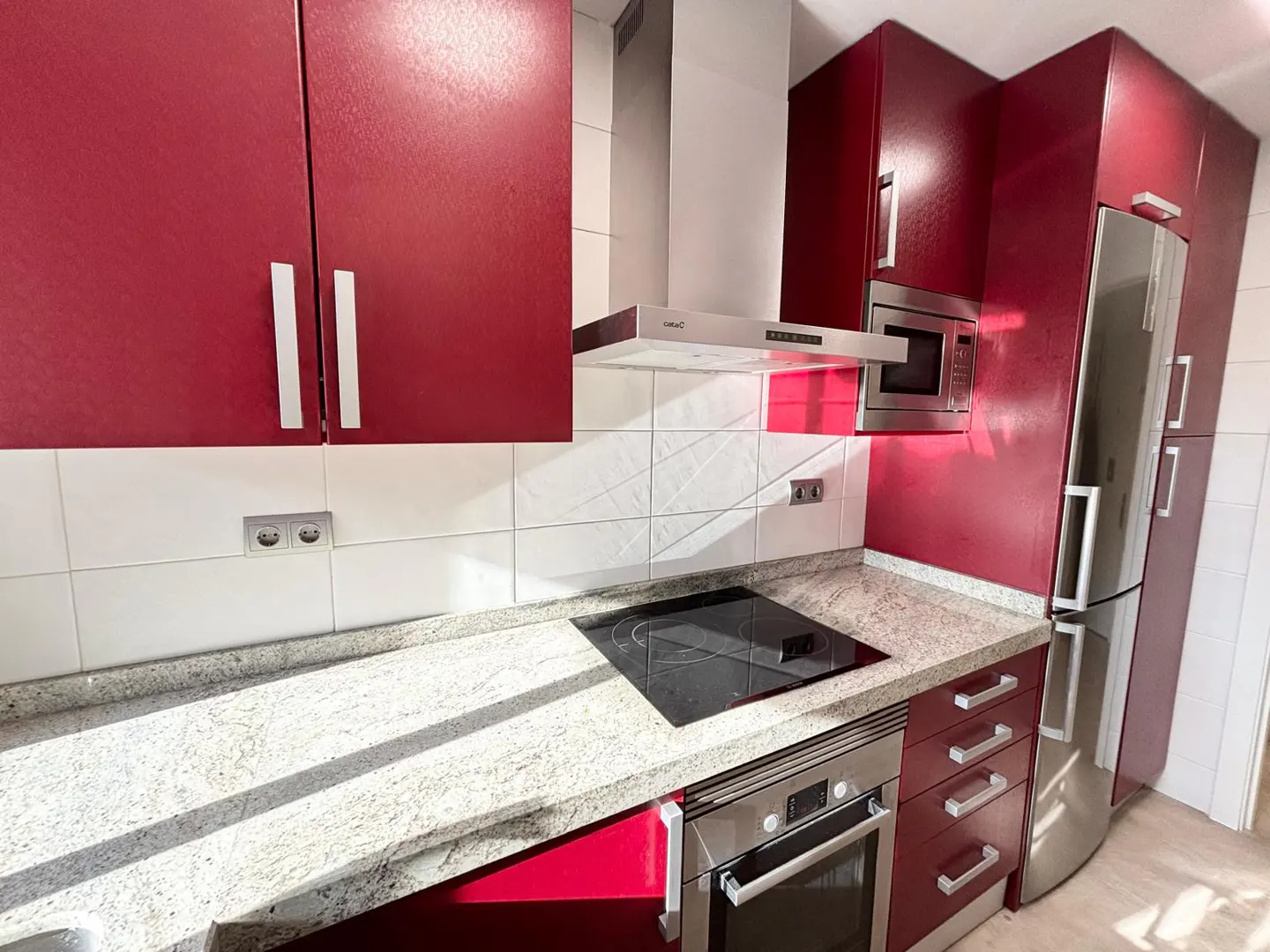 A modern kitchen with red cabinets, stainless steel appliances, and a white tile backsplash.