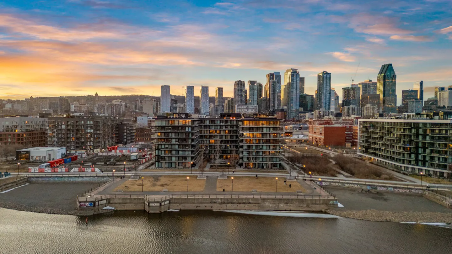 Aerial view of Montreal condos and skyline at sunset. Water in foreground, buildings and sky in background.