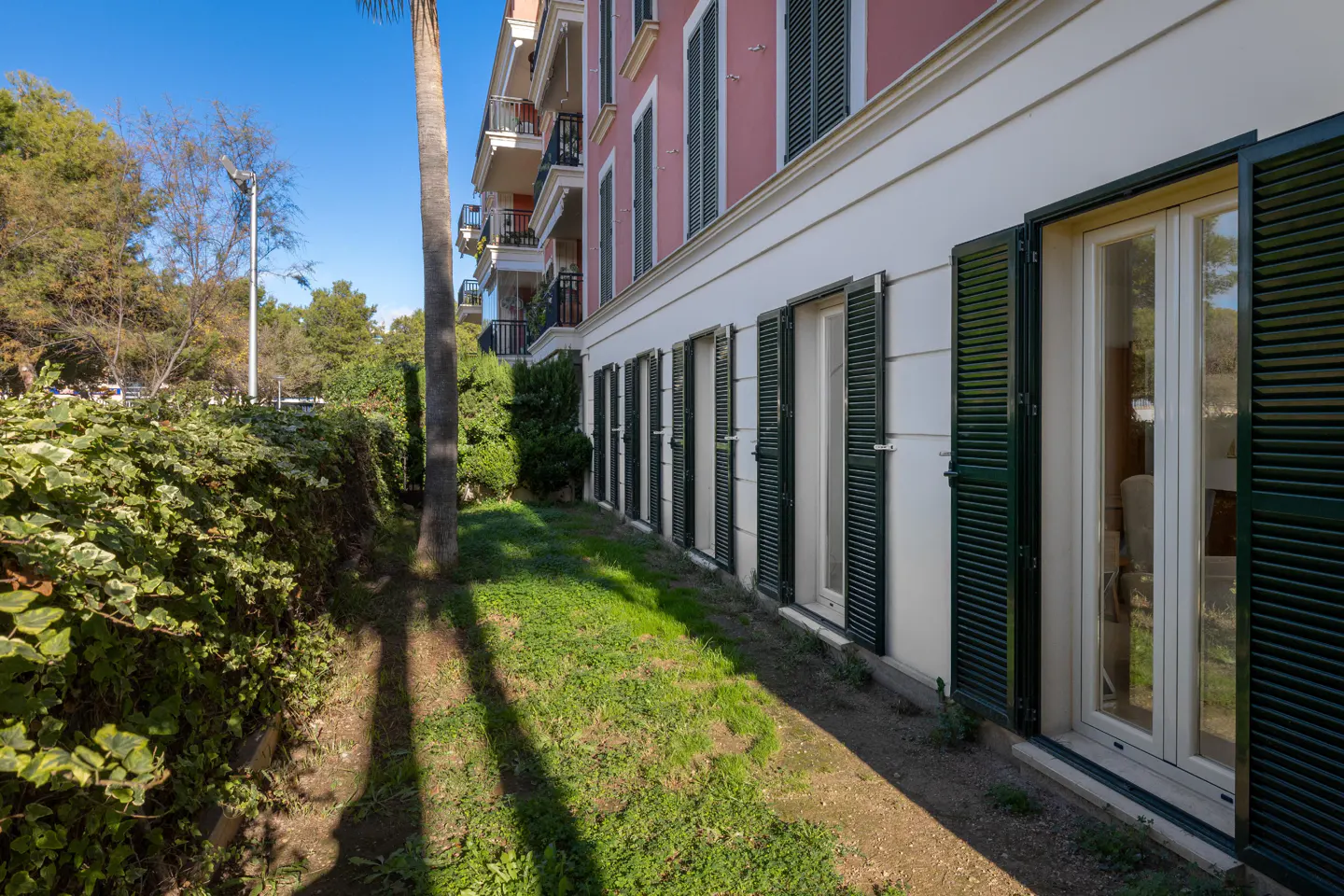 Exterior view of a pink building with green shutters and a grassy yard.