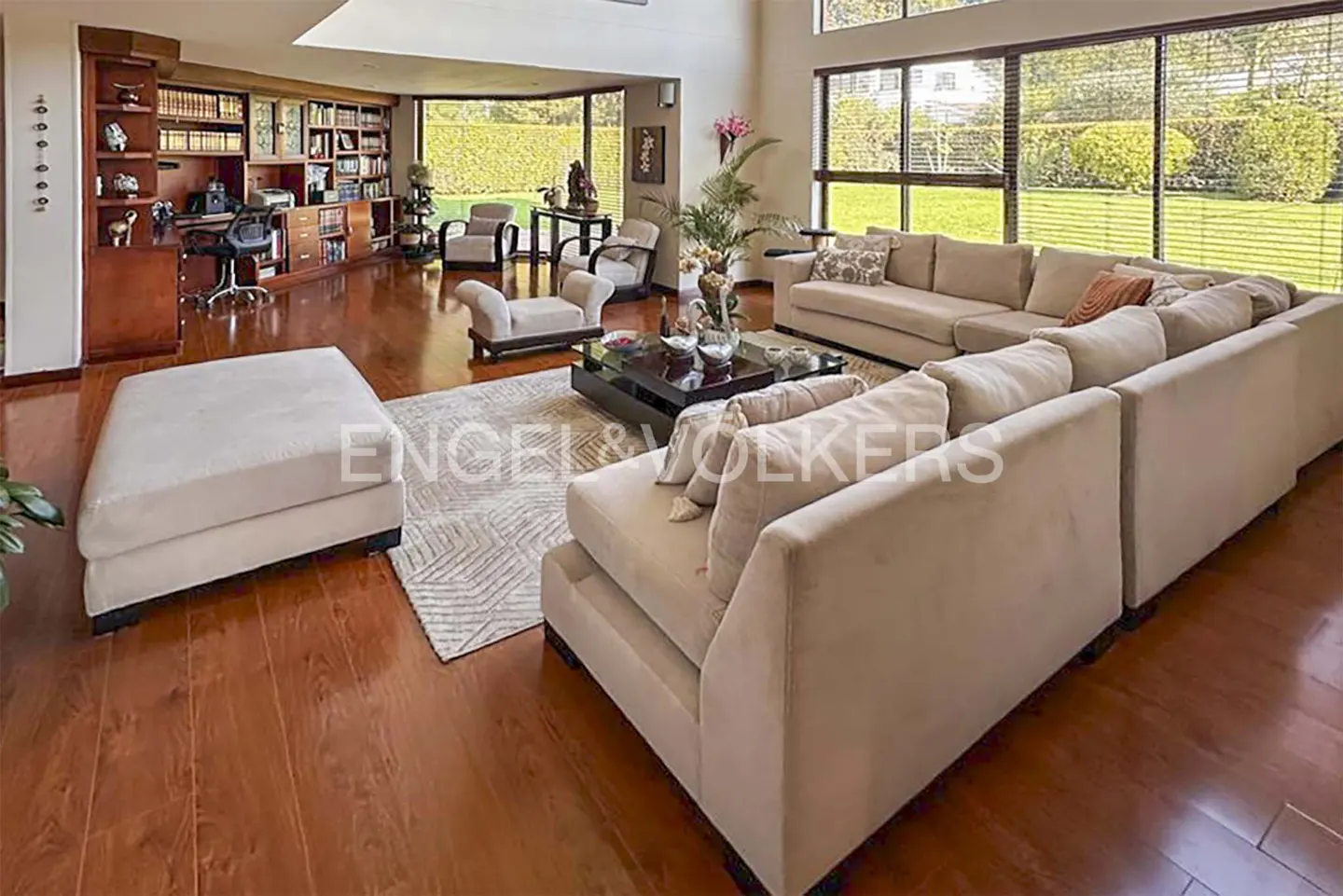 A spacious living room with a large beige sectional sofa, a dark wood floor, and a wall of bookshelves.