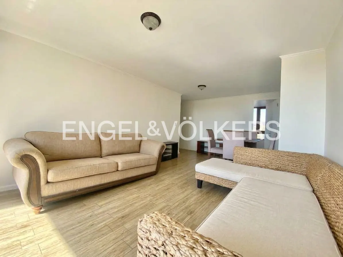 Living room with beige sofa, wicker sectional, and wood-look tile floor. Dining table and chairs visible in background. Engel & Völkers logo.