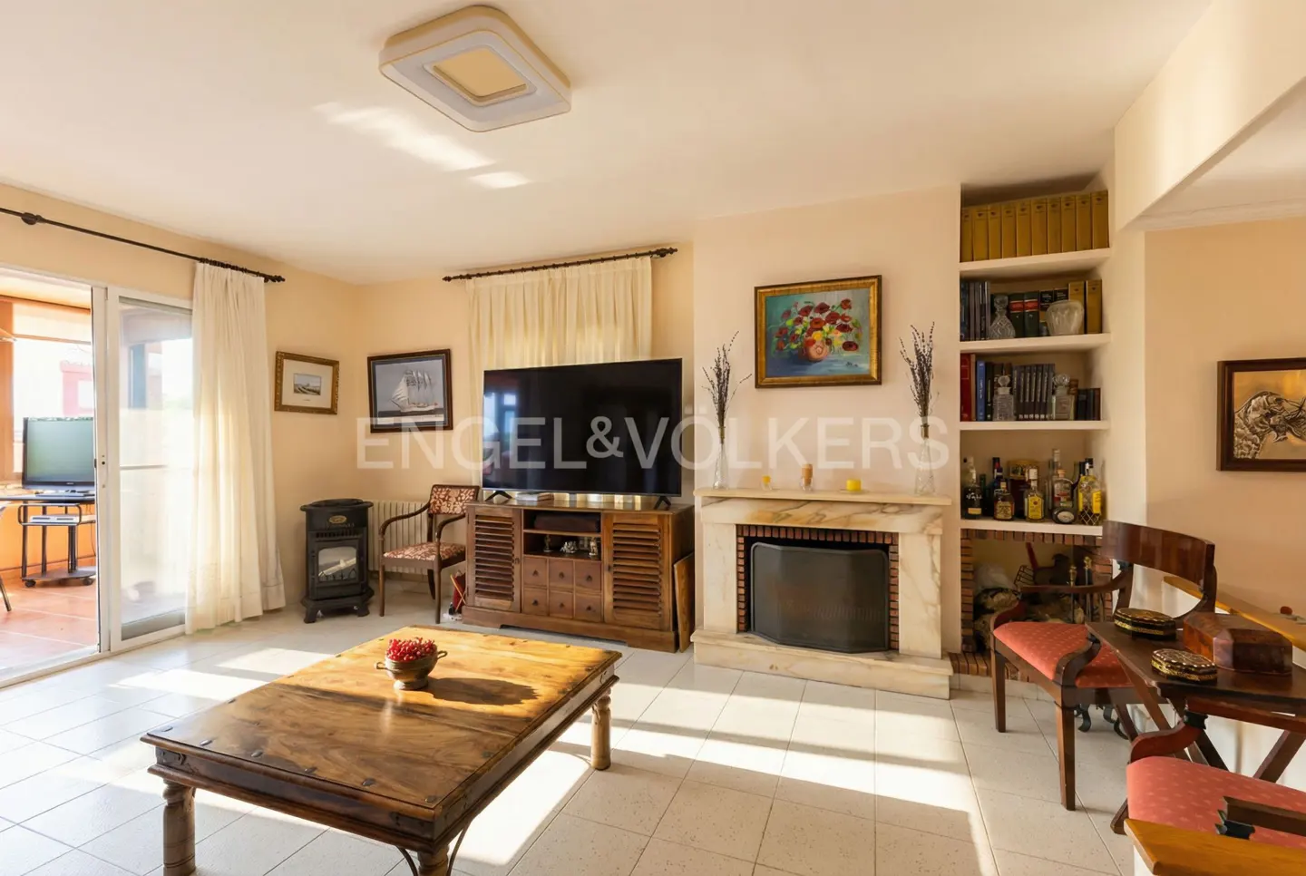 A bright living room with a fireplace, TV, wooden furniture, and a balcony with a table and chairs.