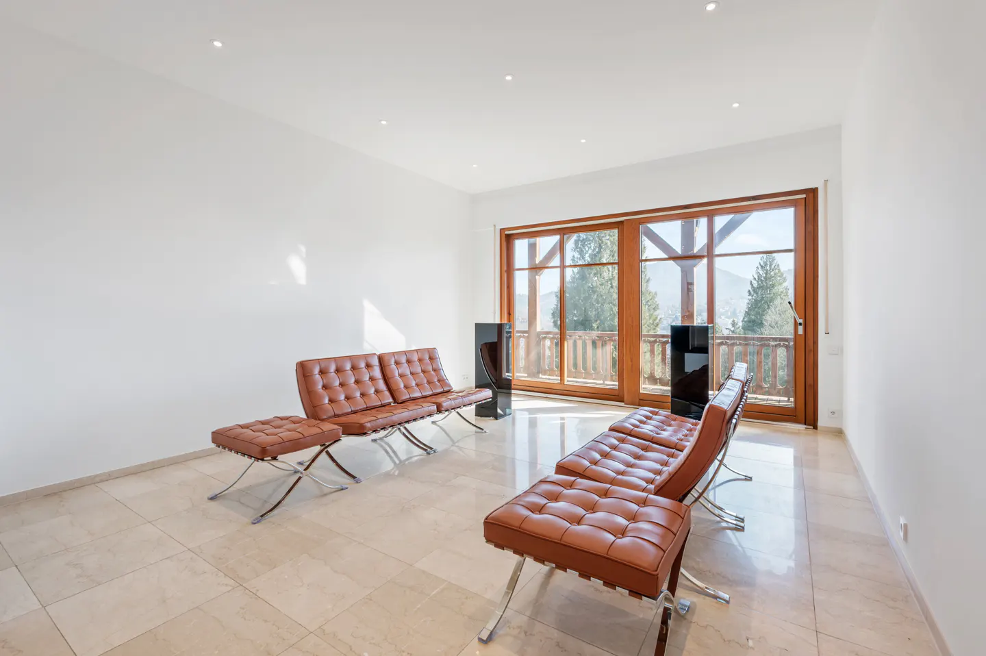 Bright room with brown leather sofas and ottomans on a marble floor. Large windows show a mountain view.