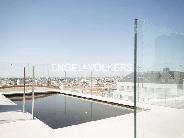 Rooftop infinity pool with a glass railing overlooking a sprawling city skyline under a clear blue sky.