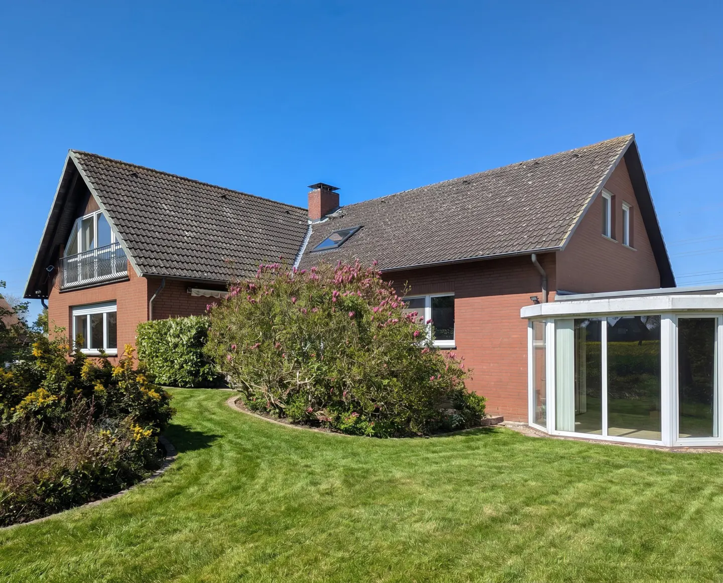 A brick house with a gray tiled roof, a sunroom, and a green lawn under a clear blue sky.