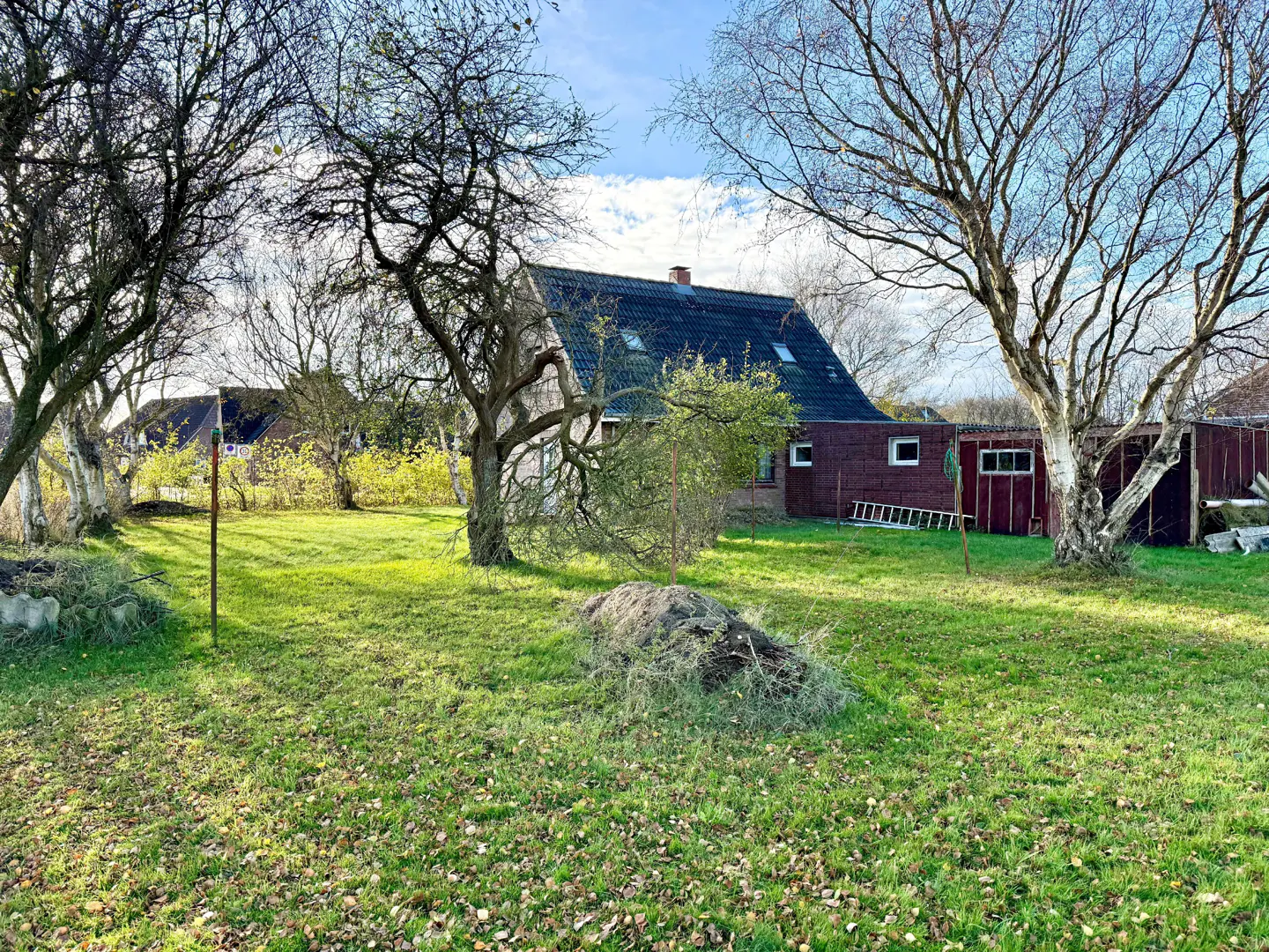 A view of a green lawn with trees and a red brick house with a dark roof in the background.