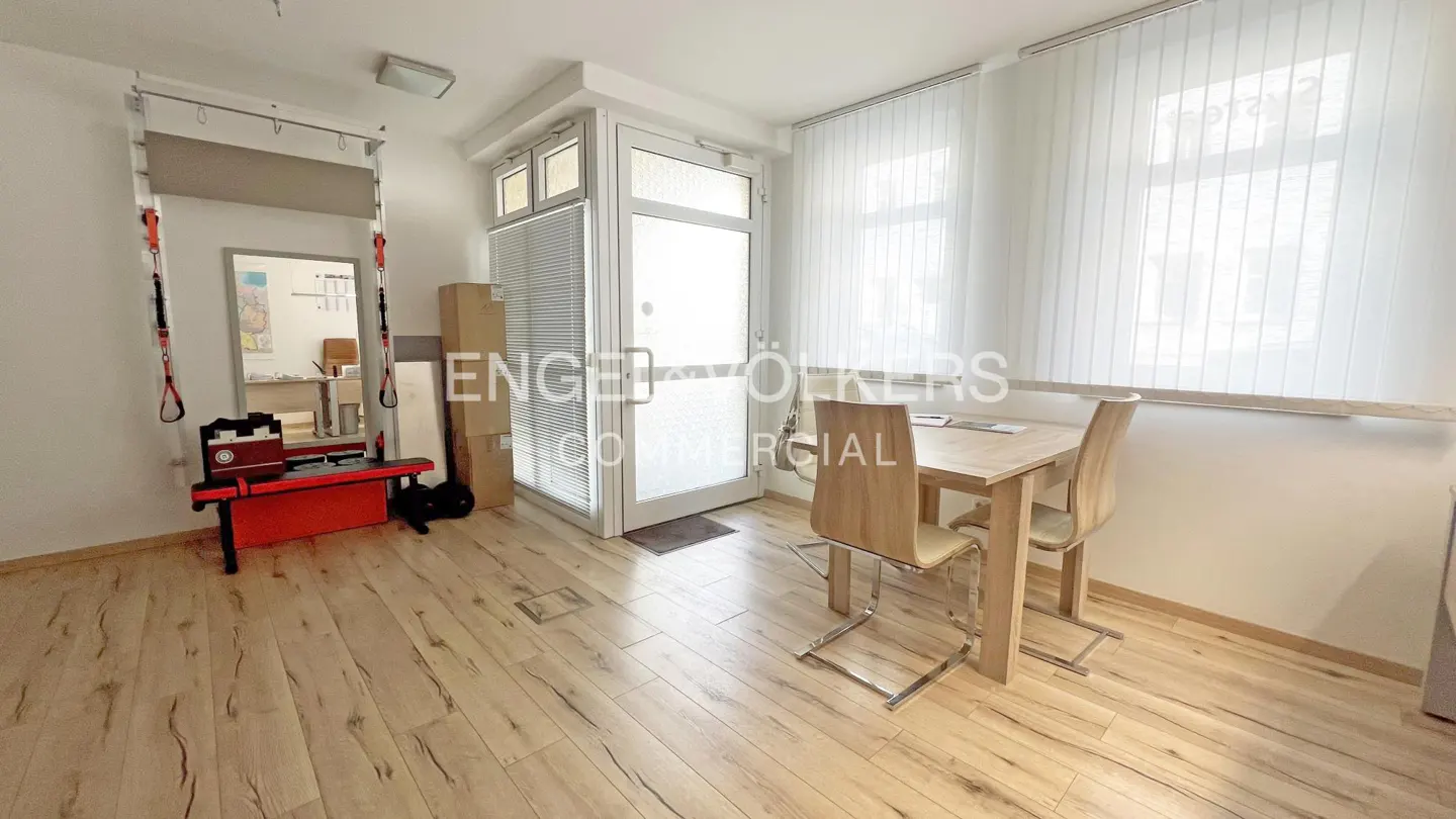 A bright room with wood floors, a table with two chairs, and exercise equipment. A glass door and windows with white blinds are visible.