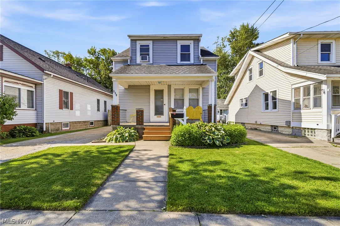 Two-story light blue house with a front porch, yellow chairs, and a green lawn under a clear blue sky.