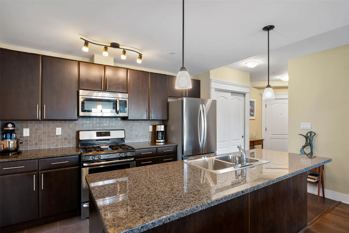 A modern kitchen with dark brown cabinets, stainless steel appliances, and a granite countertop island with a sink.
