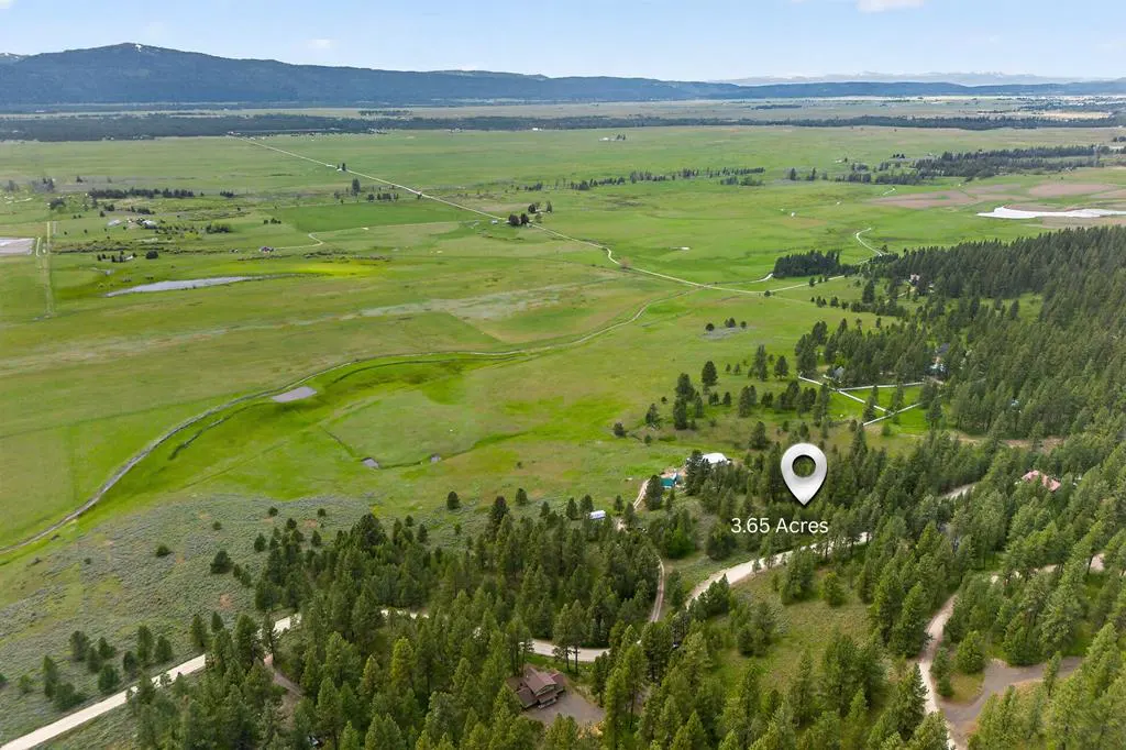 Aerial view of 3.65 acres of land with green fields, trees, and a mountain range in the background. A white pin marks the property.