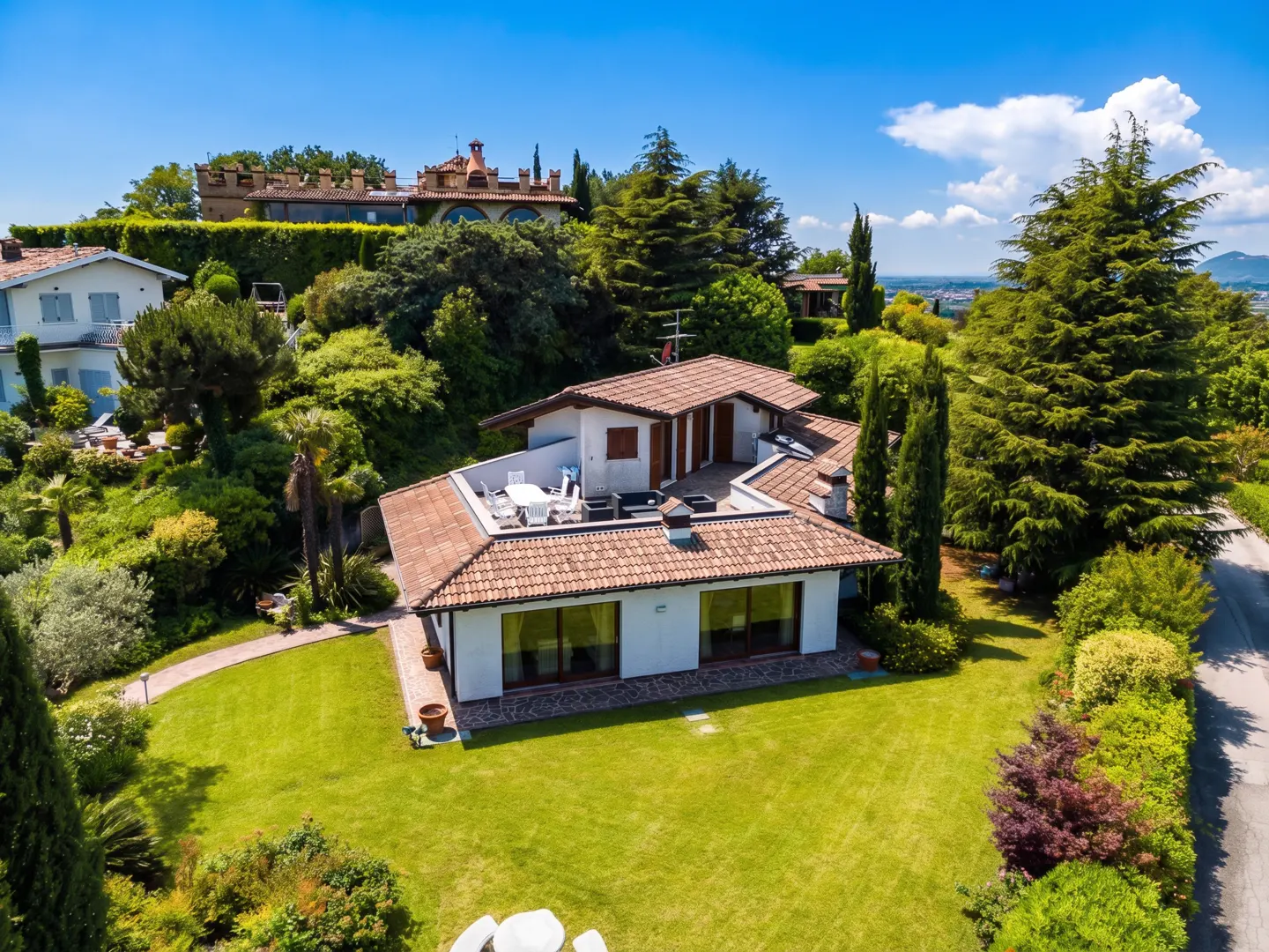 Aerial view of a white house with a red tile roof, green lawn, and trees under a blue sky.