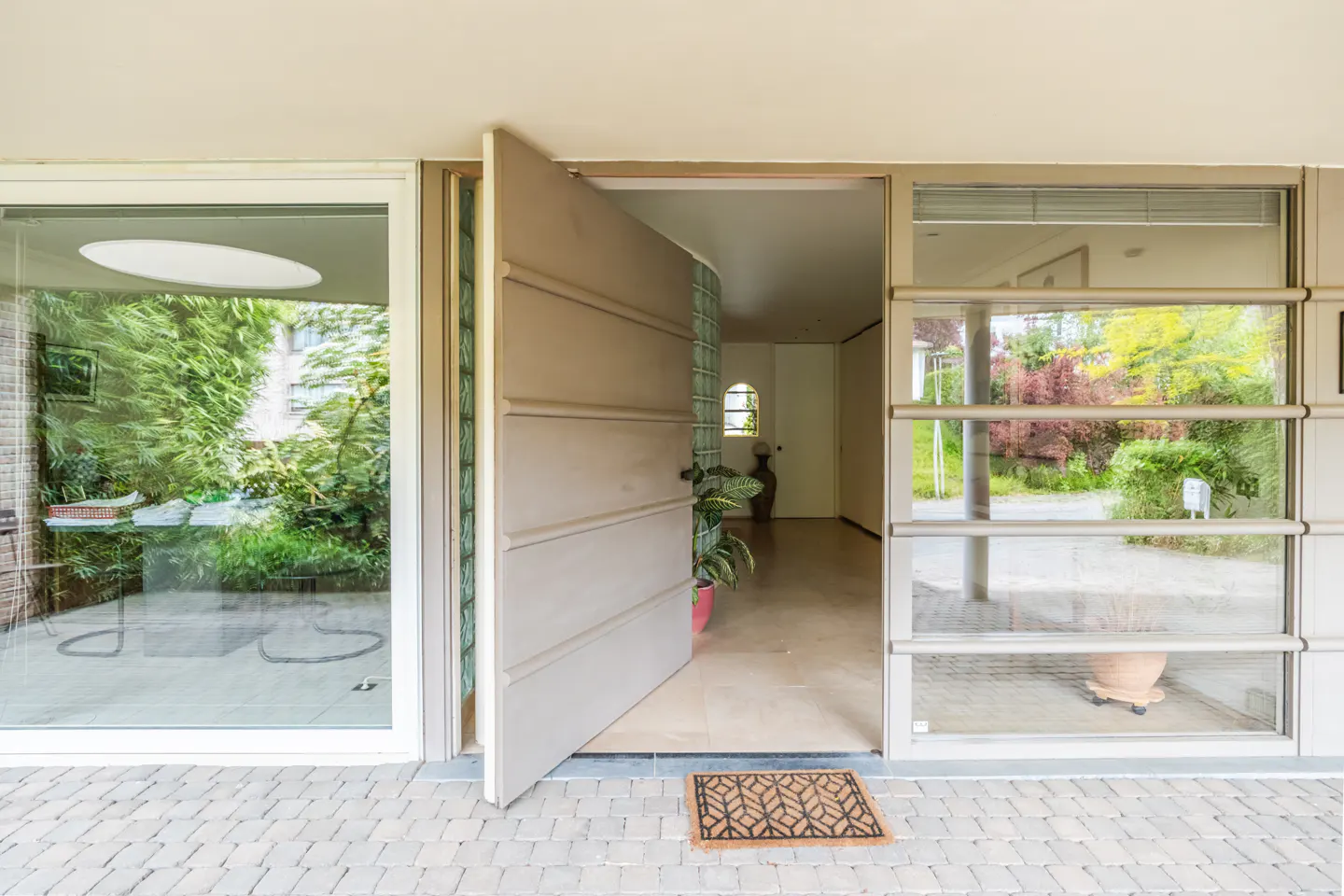 Open front door of a modern home with large windows, a brown doormat, and a view into the house.