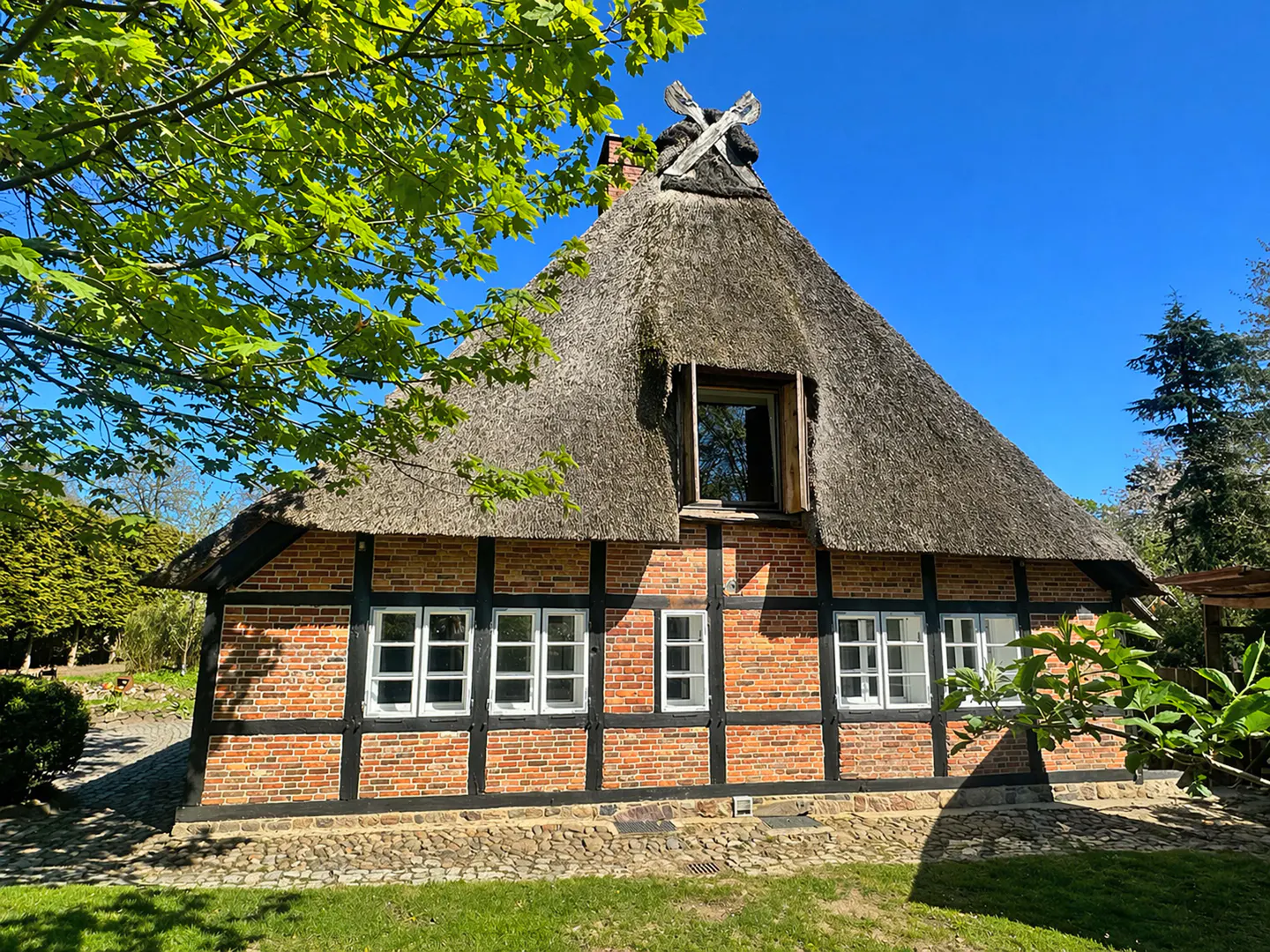 Exterior of a red brick house with a thatched roof and white framed windows.