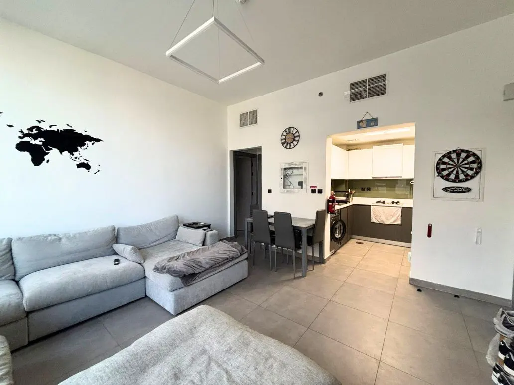 A wide shot of a modern apartment with a gray sectional sofa, dining table, and open kitchen. A world map decal is on the wall.