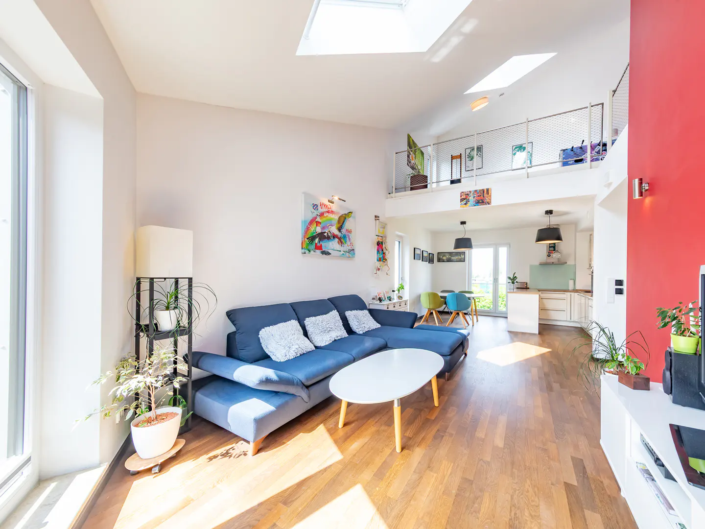 Bright, modern living room with a blue sectional sofa, white coffee table, and hardwood floors. Skylights and a loft area add architectural interest.