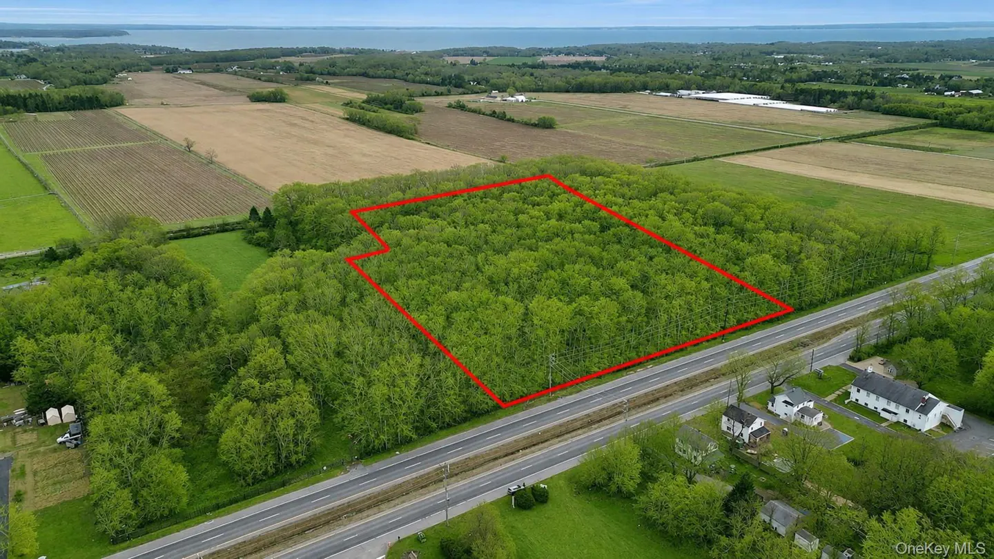 Aerial view of a wooded property outlined in red, adjacent to a road with houses and farmland in the background.