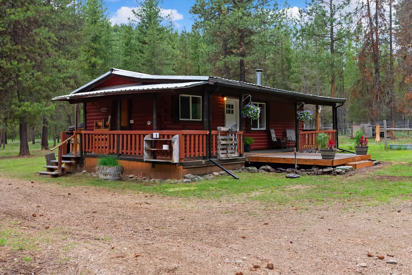 Rustic log cabin with a red porch and metal roof, surrounded by tall green trees.