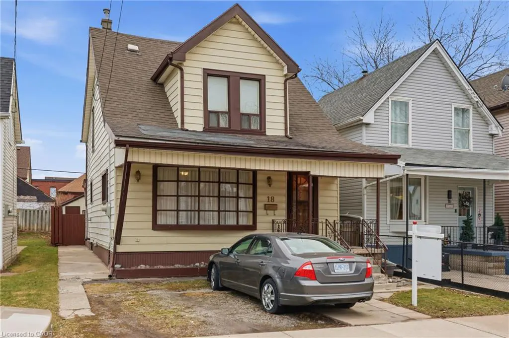Two-story house with beige siding, brown trim, and a brown roof. A gray car is parked in front. Number 18 is on the house.