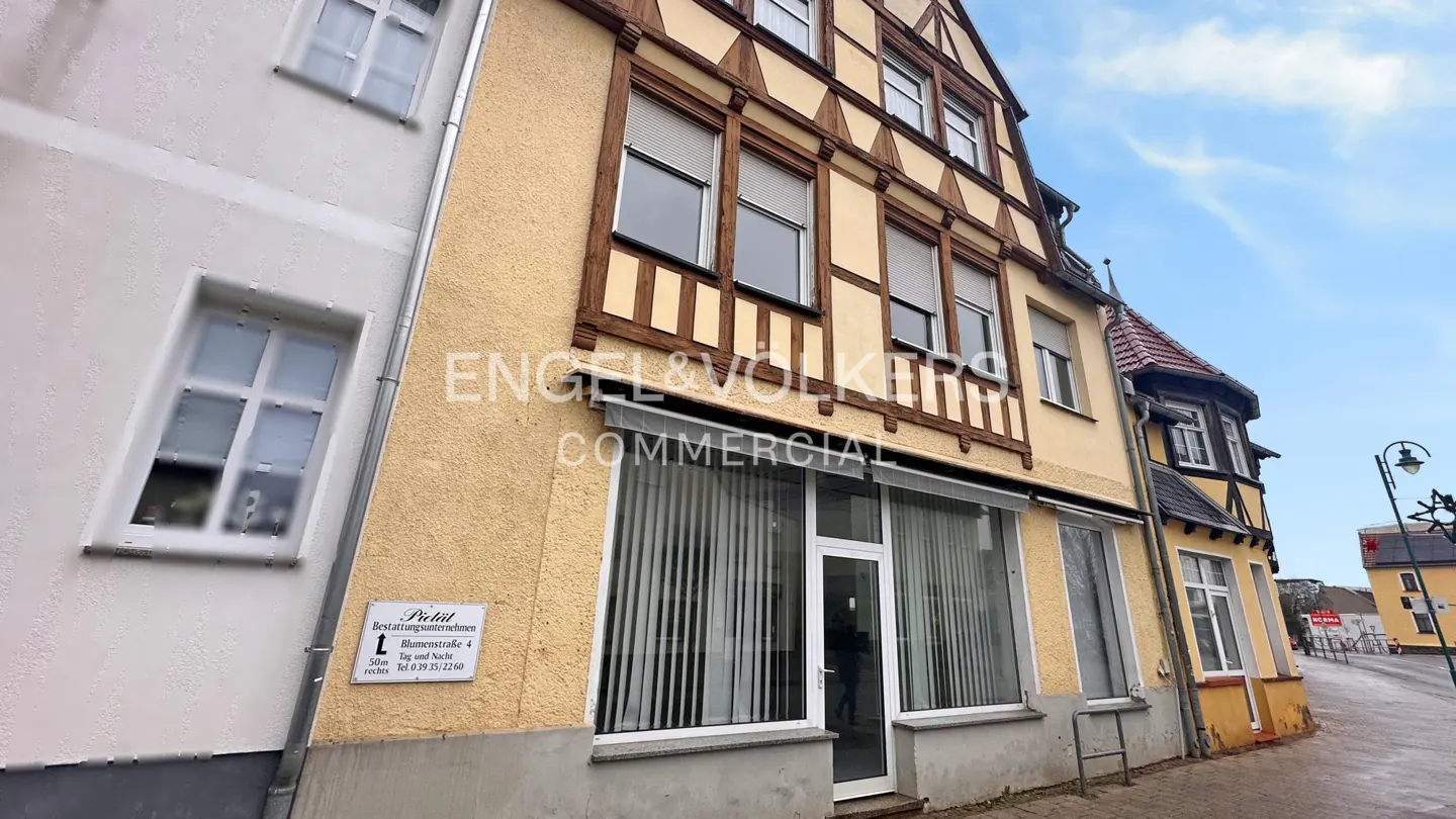 Exterior of a yellow and brown half-timbered building with Engel & Volkers Commercial sign. Windows have white blinds.