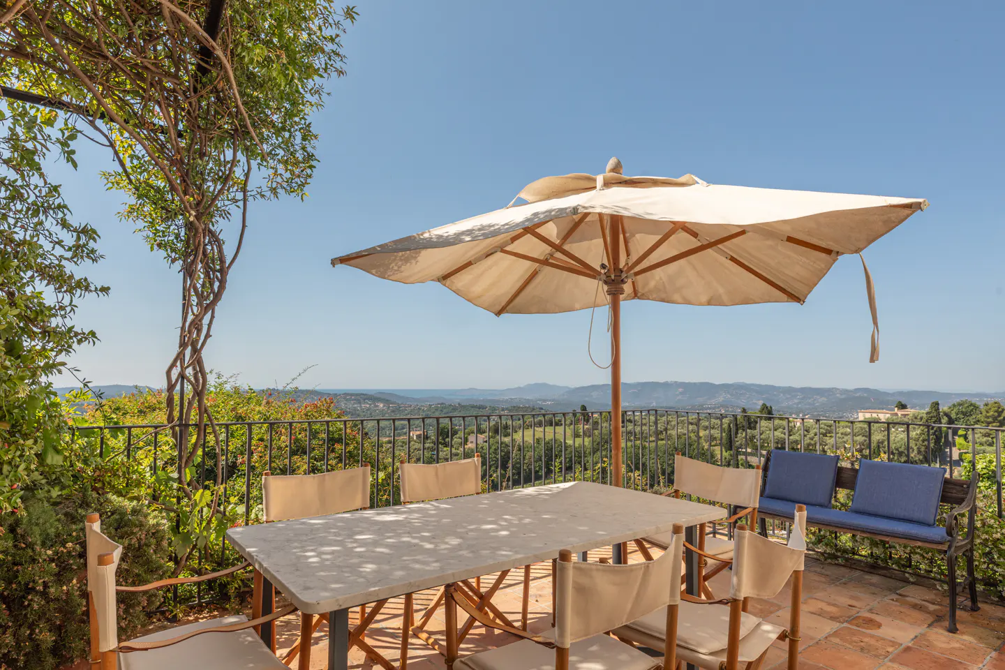 Outdoor patio with a table, chairs, and umbrella overlooking a scenic landscape with trees and mountains in the distance.